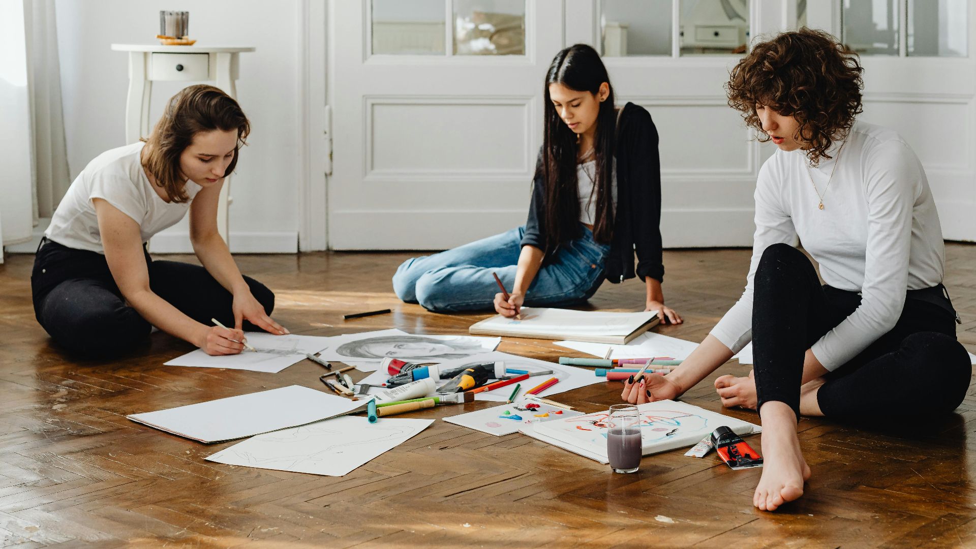Three women sitting on the floor engaged in creative artwork in a bright, modern room.