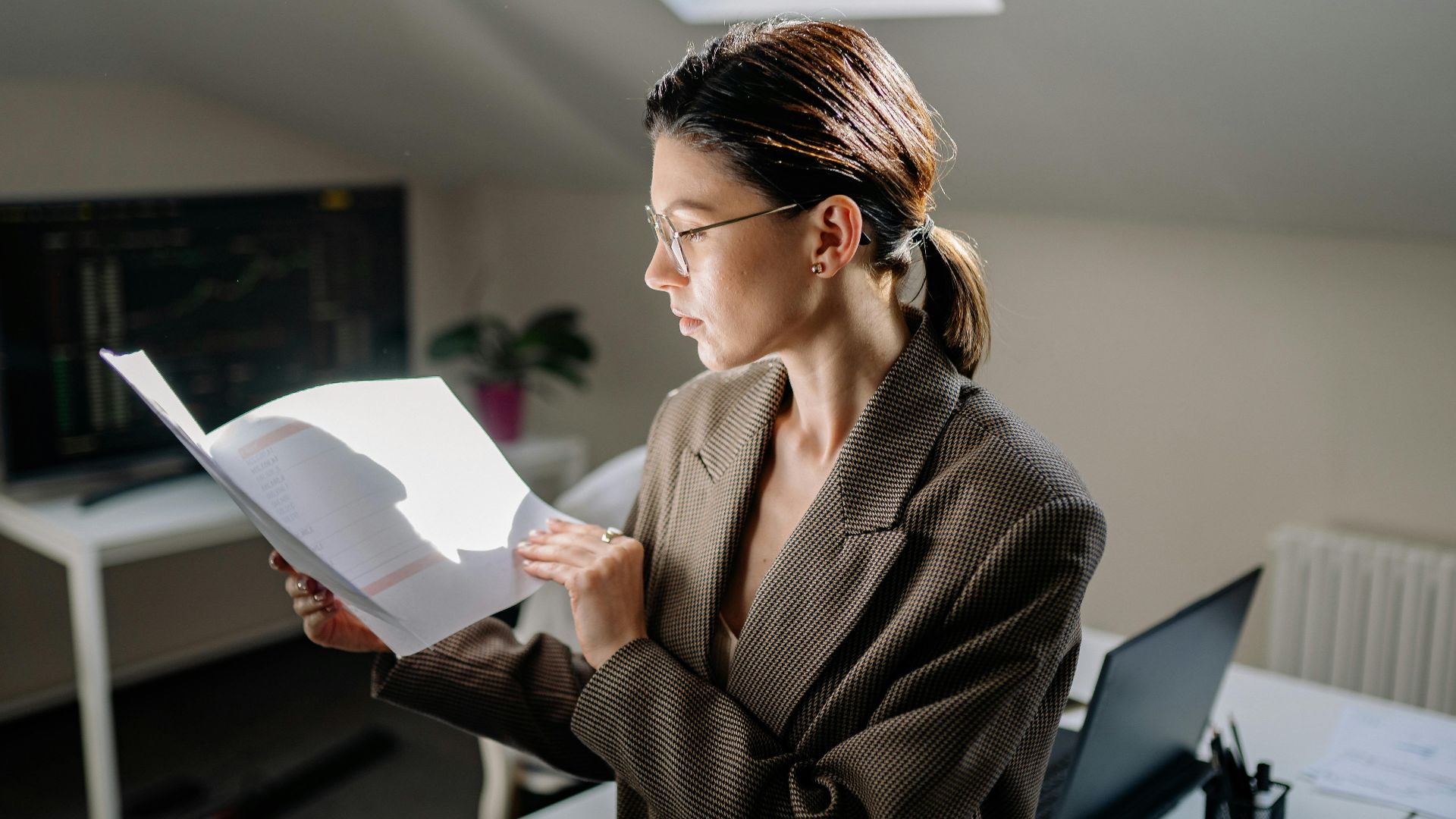 Professional woman in glasses reviewing financial documents at her office desk.