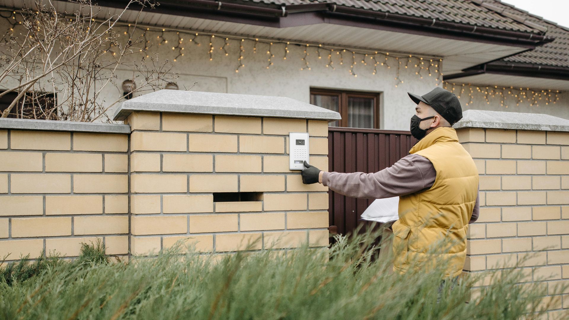 A delivery worker wearing a face mask presses a doorbell at a residential home, emphasizing contactless service.