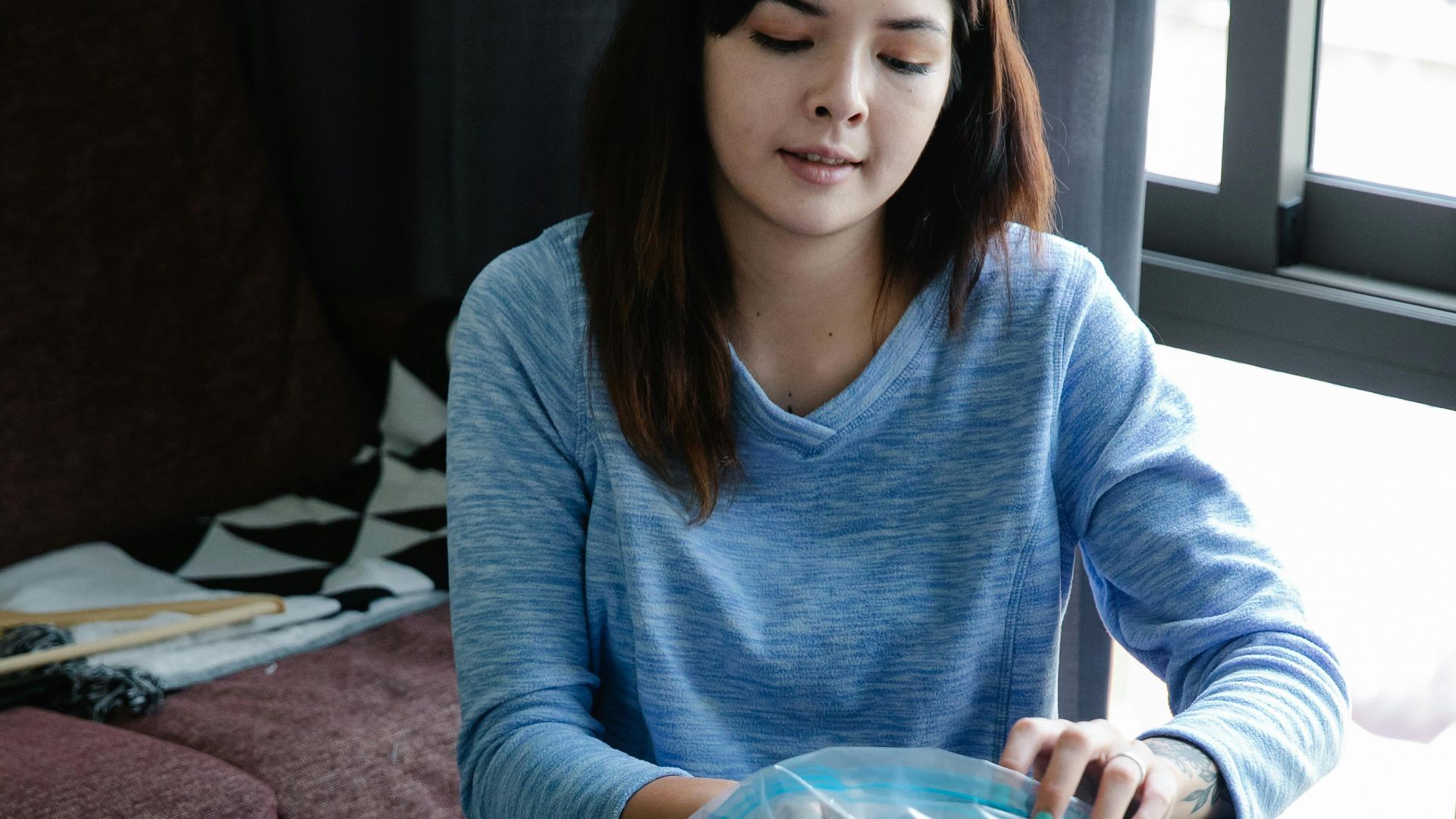 Young woman using vacuum seal bags to pack clothes indoors.