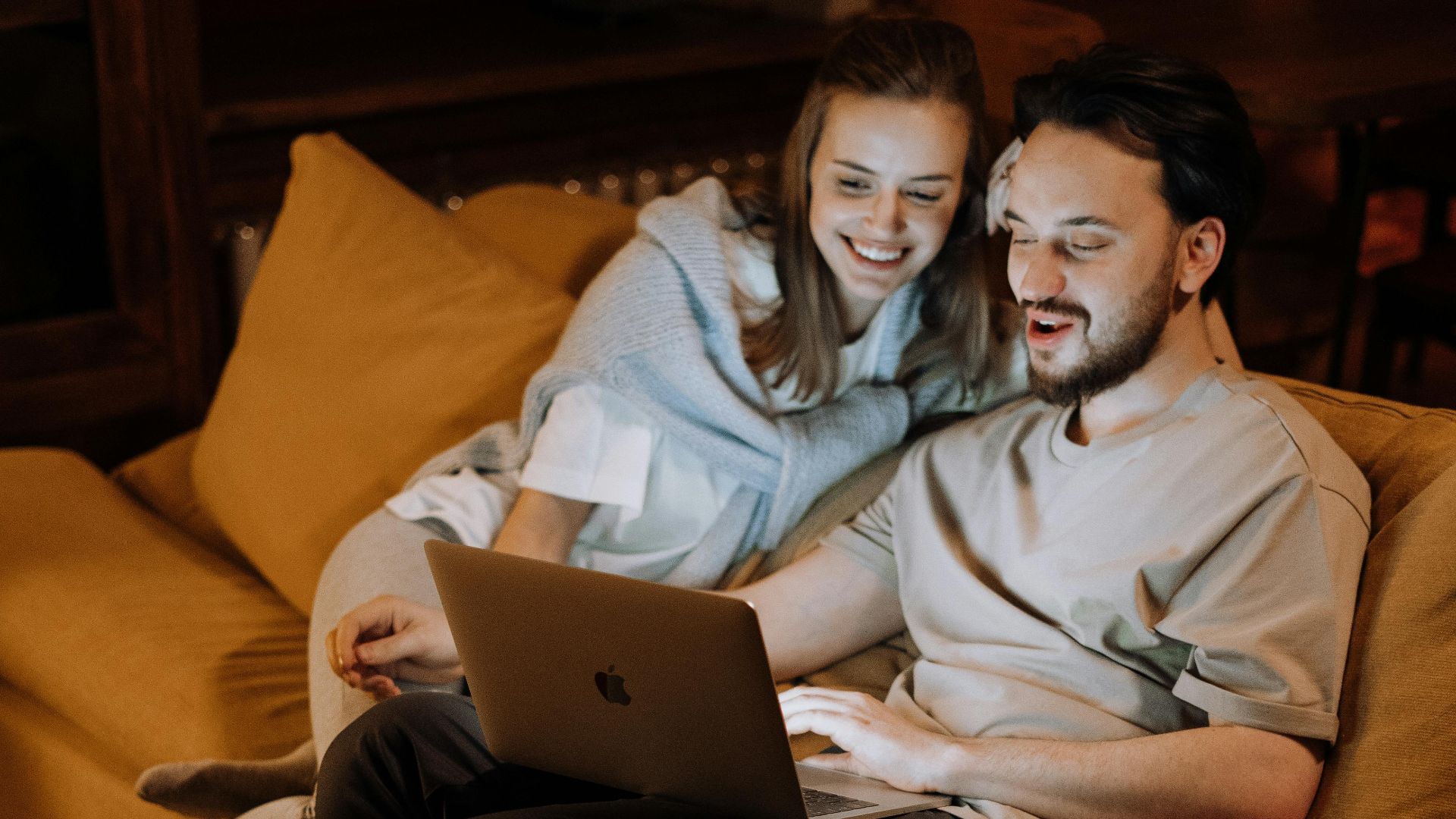 A couple relaxing on a cozy sofa at home using a laptop during the evening.
