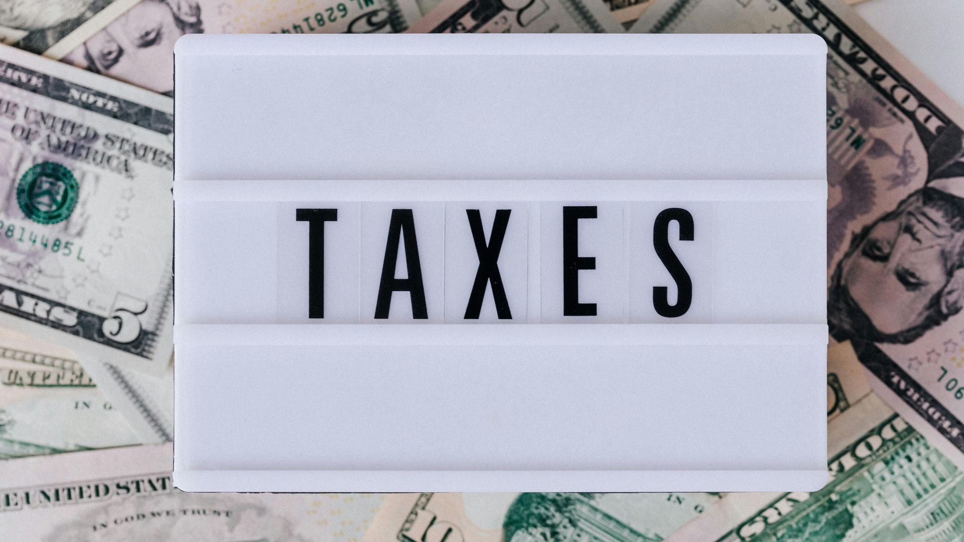 Top view of white vintage light box with TAXES inscription placed on stack of USA dollar bills on white surface
