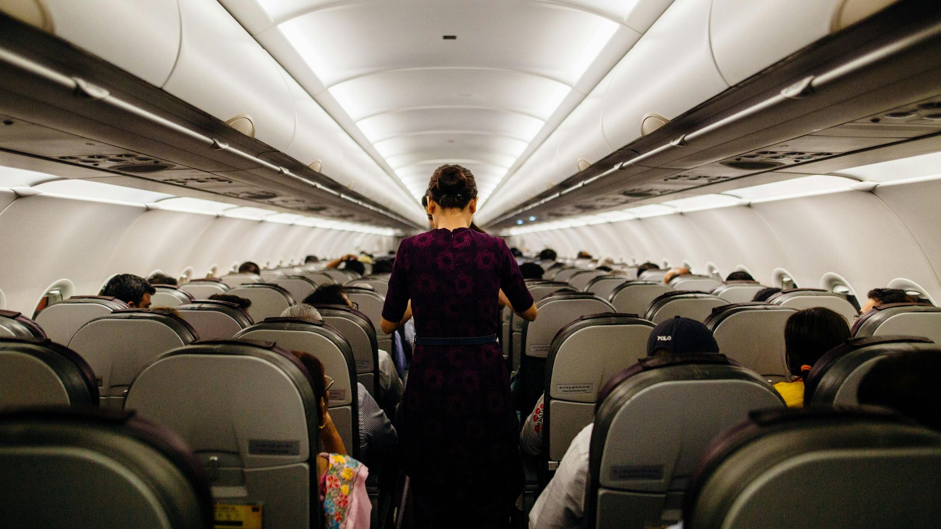 Interior view of an airplane cabin with passengers seated and a flight attendant walking down the aisle.