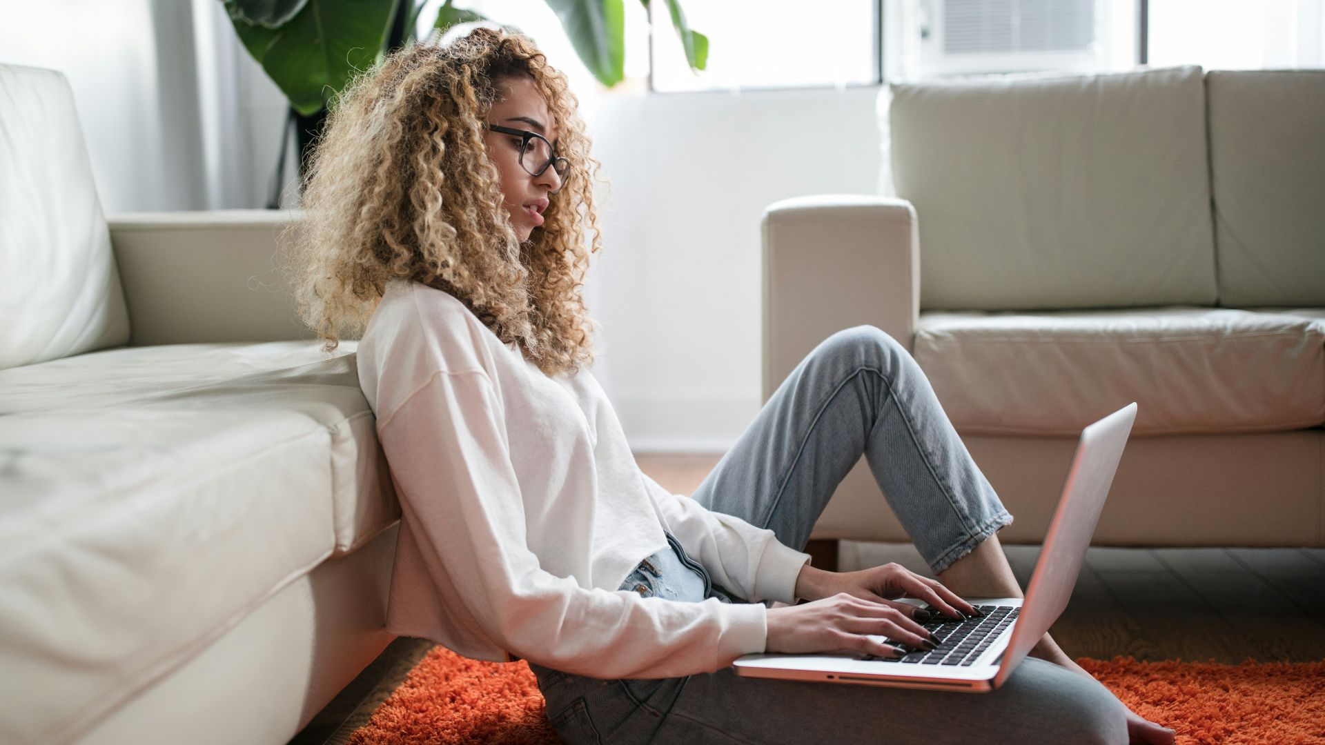 woman sitting on floor and leaning on couch using laptop