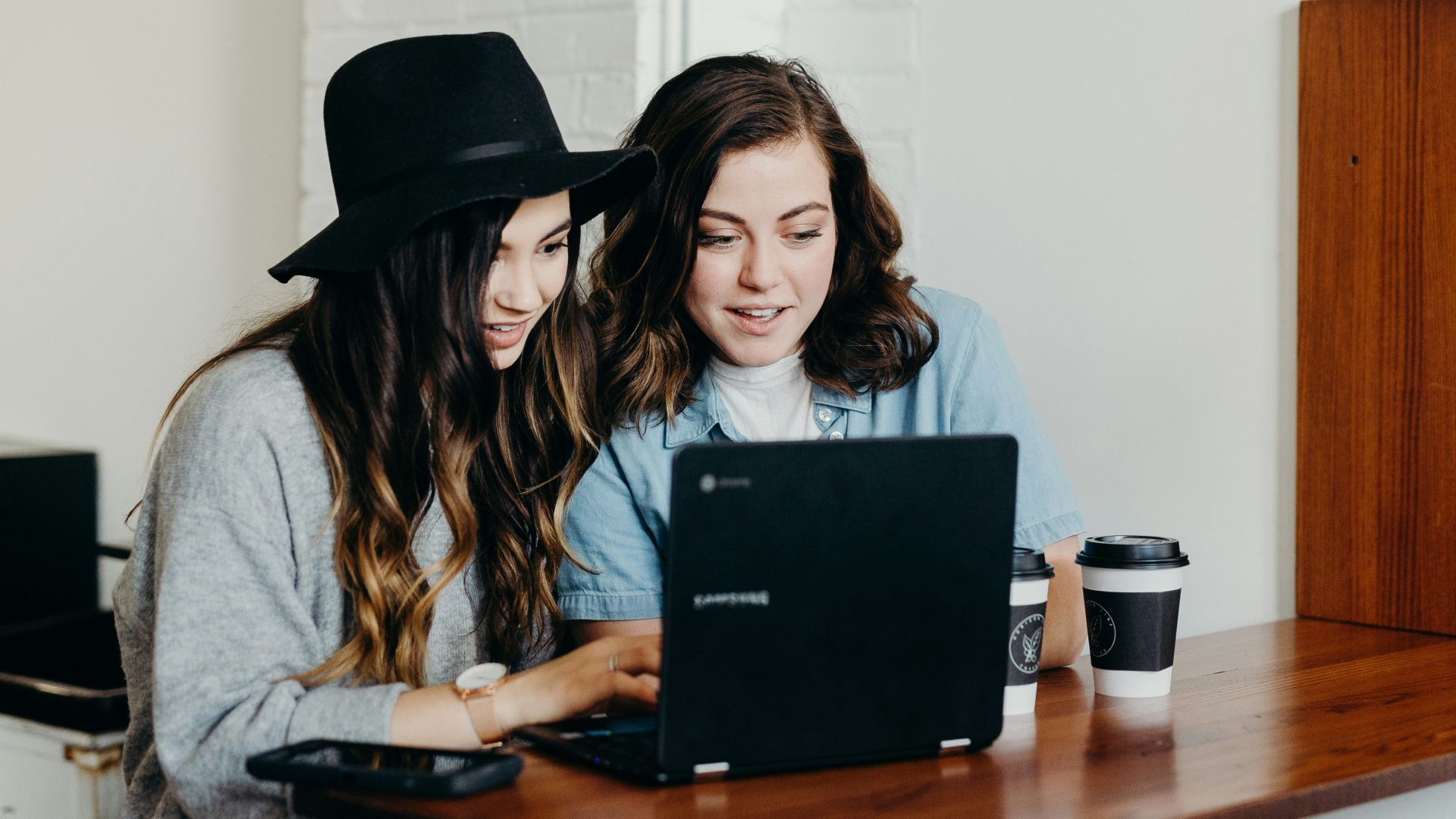 two woman sitting near table using Samsung laptop