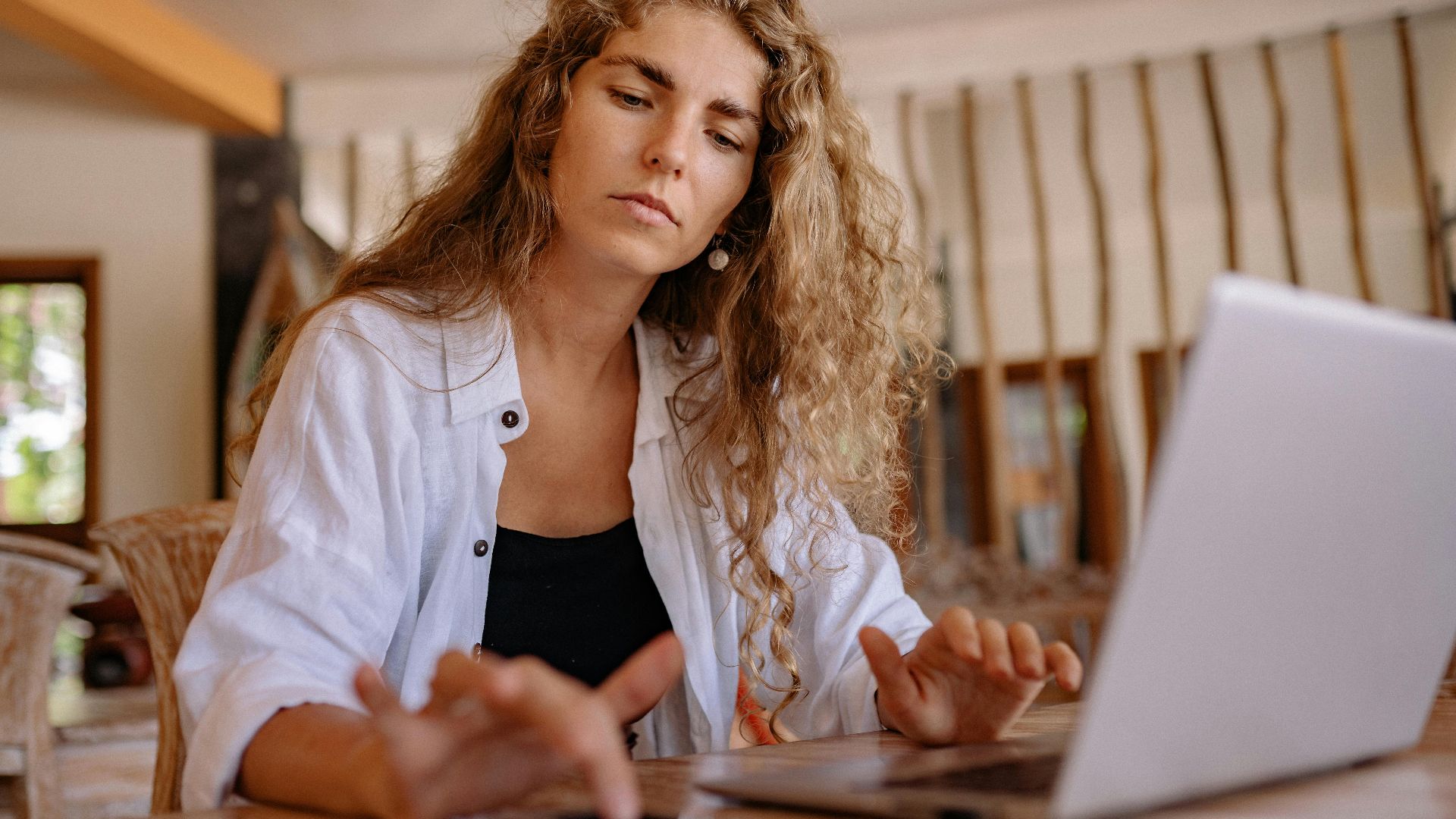 A woman intently works on a laptop while using a smartphone indoors, symbolizing modern remote work.