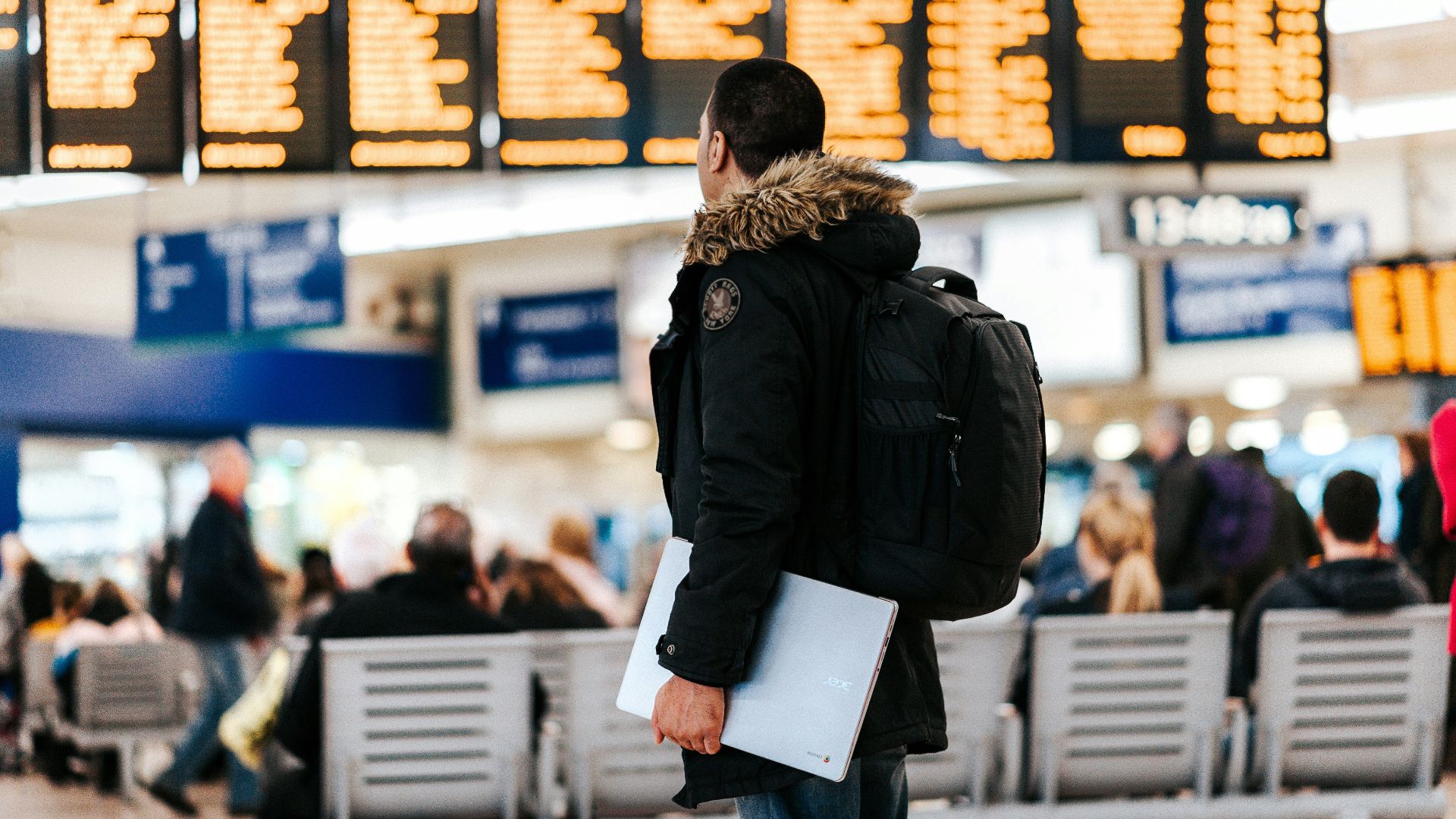 man standing inside airport looking at LED flight schedule bulletin board