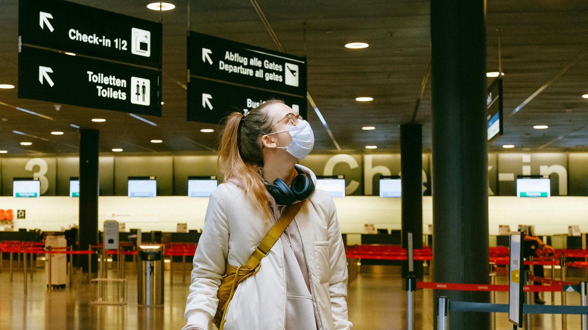 A woman in a face mask stands with her luggage in an empty airport terminal.