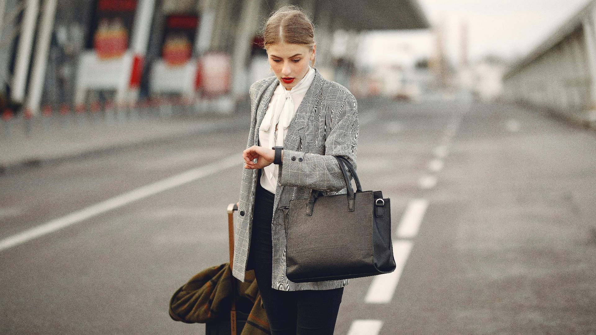 A businesswoman checks her watch while waiting at an airport terminal, looking concerned.