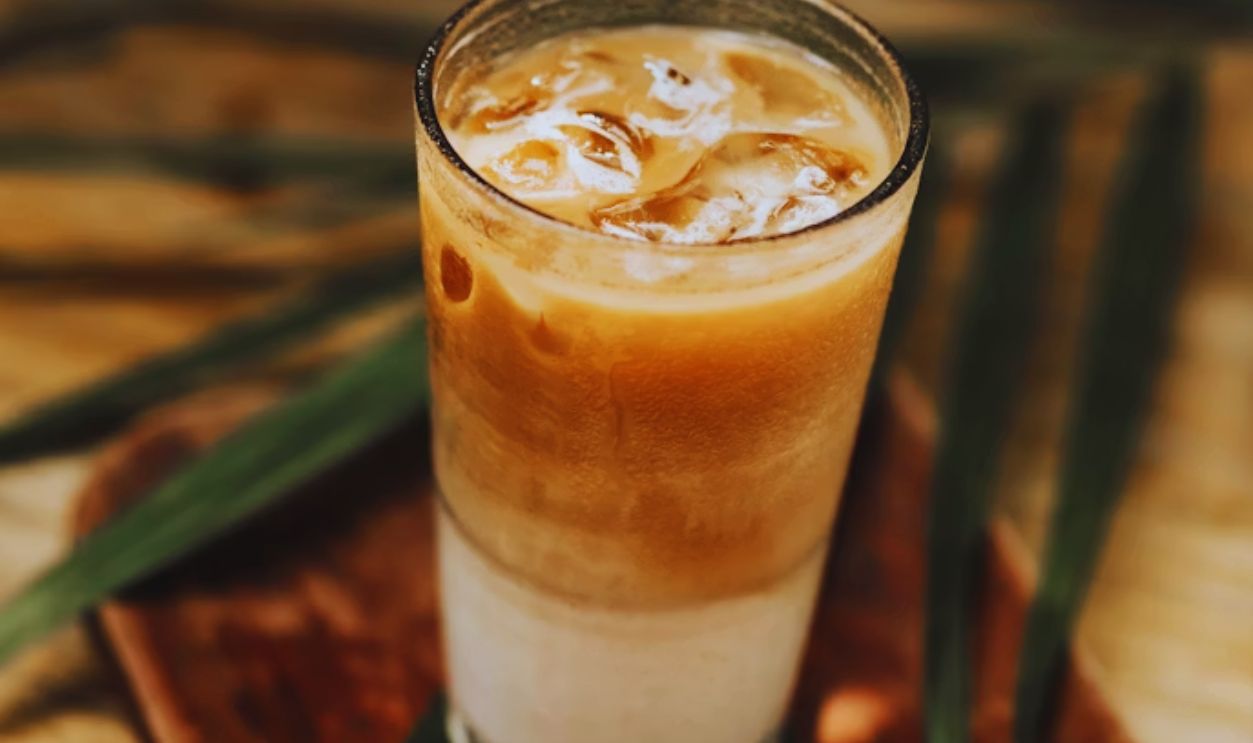 a glass of iced coffee sitting on top of a wooden tray