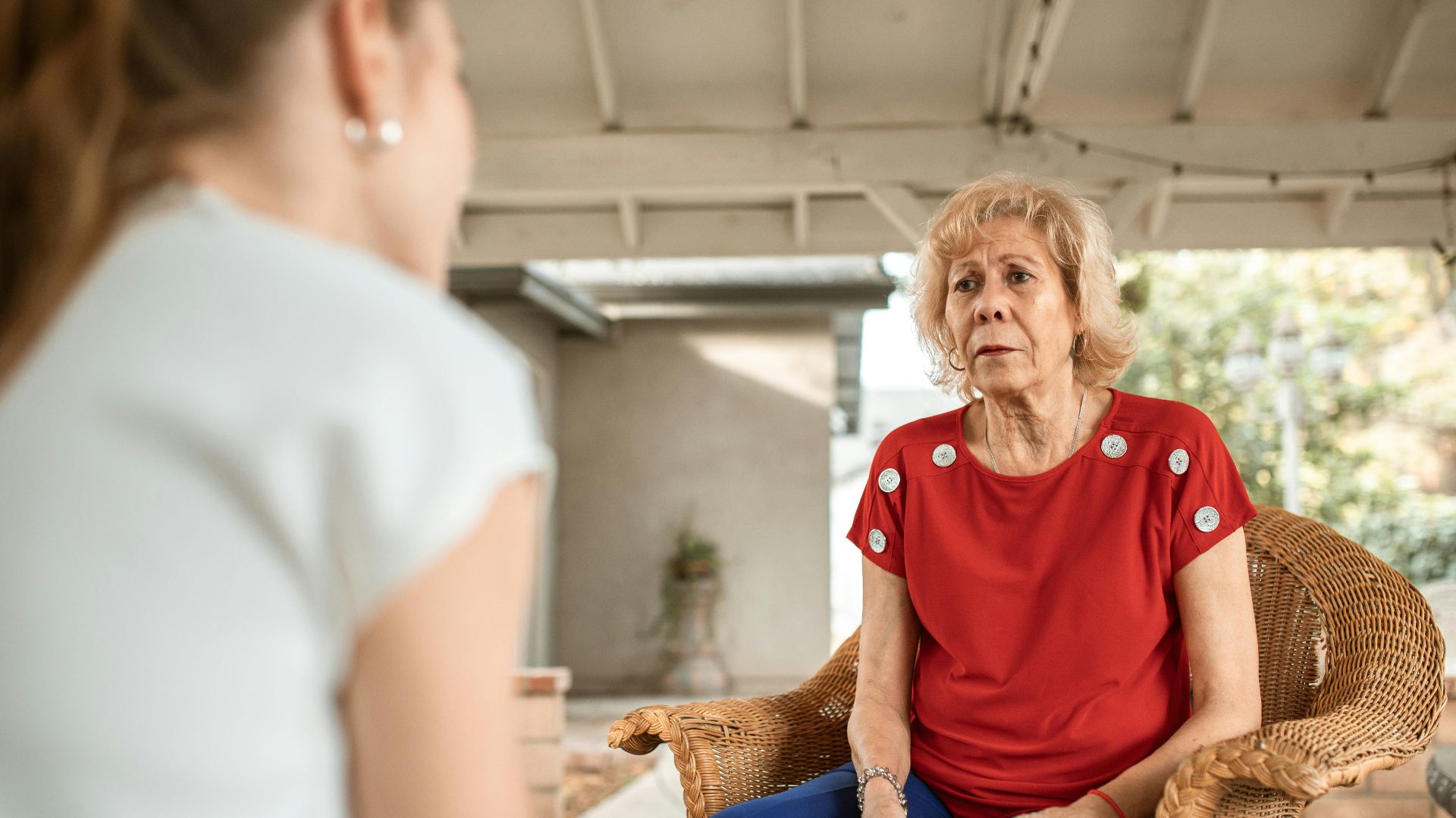 Senior woman in red shirt conversing indoors with younger woman. Daytime scene.