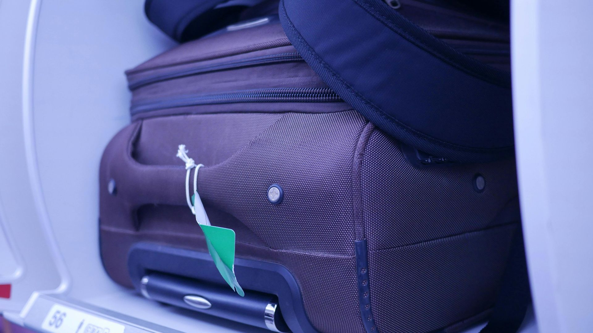 Close-up of luggage in an airplane's overhead compartment, showcasing travel essentials.