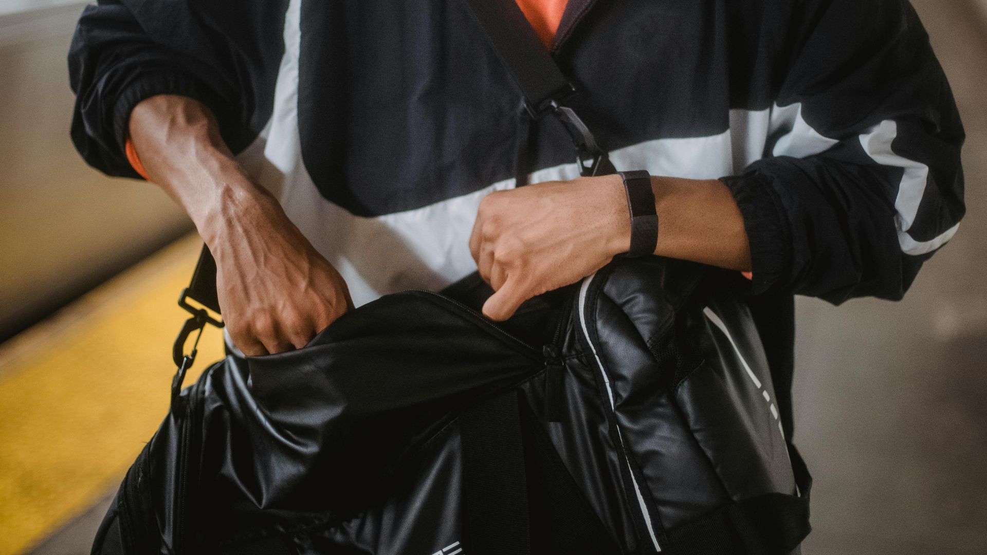 A close-up of a man in sports clothing searching his bag on a train station platform.