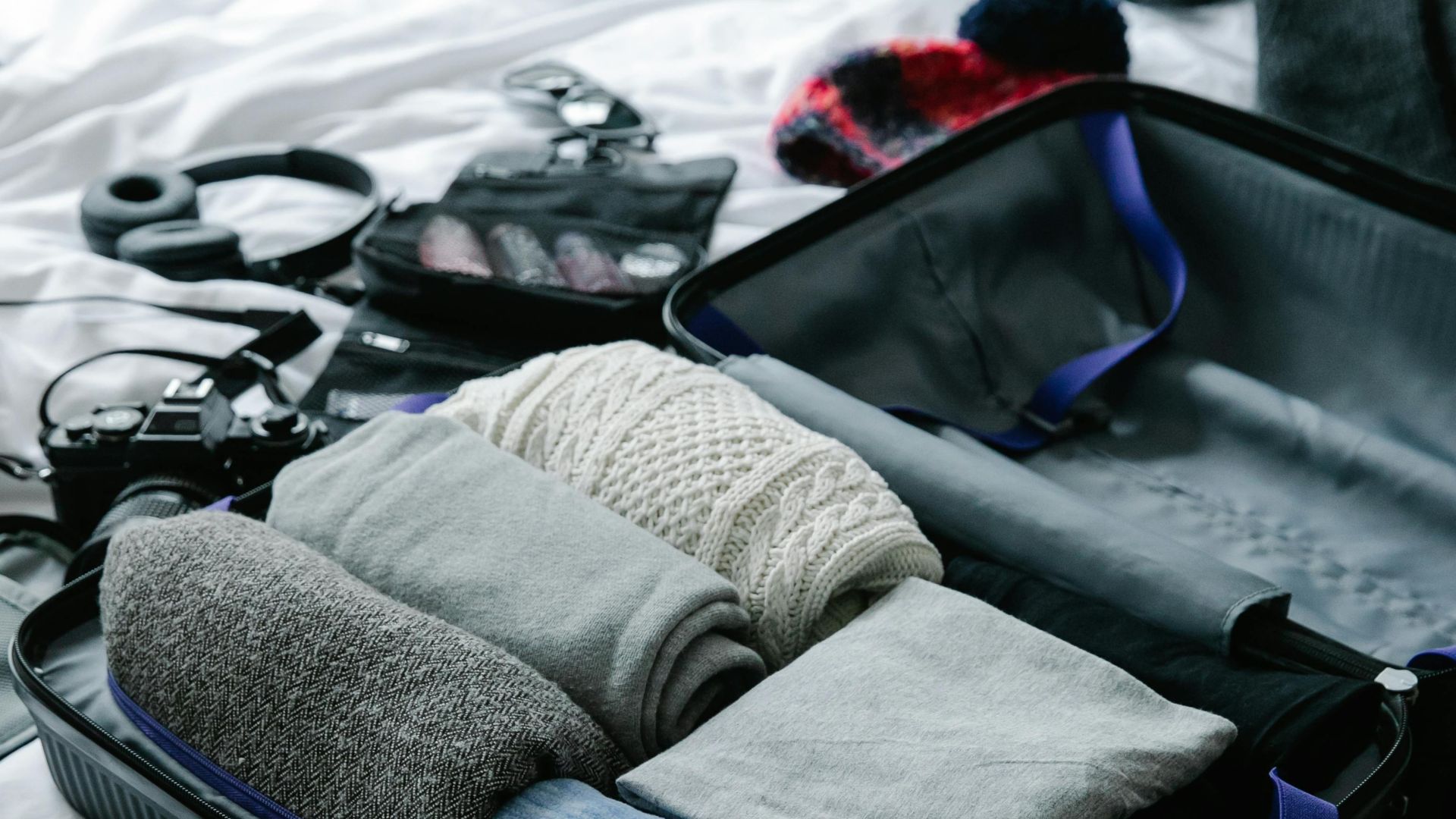 Open suitcase filled with neatly folded clothes on bed, ready for travel preparation.