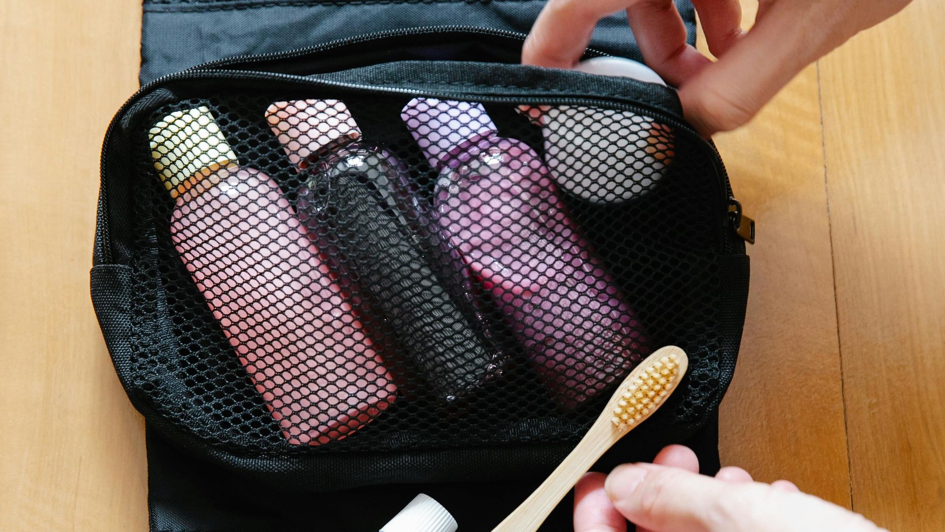 Open toiletry bag with bottles and a bamboo toothbrush on wooden surface.