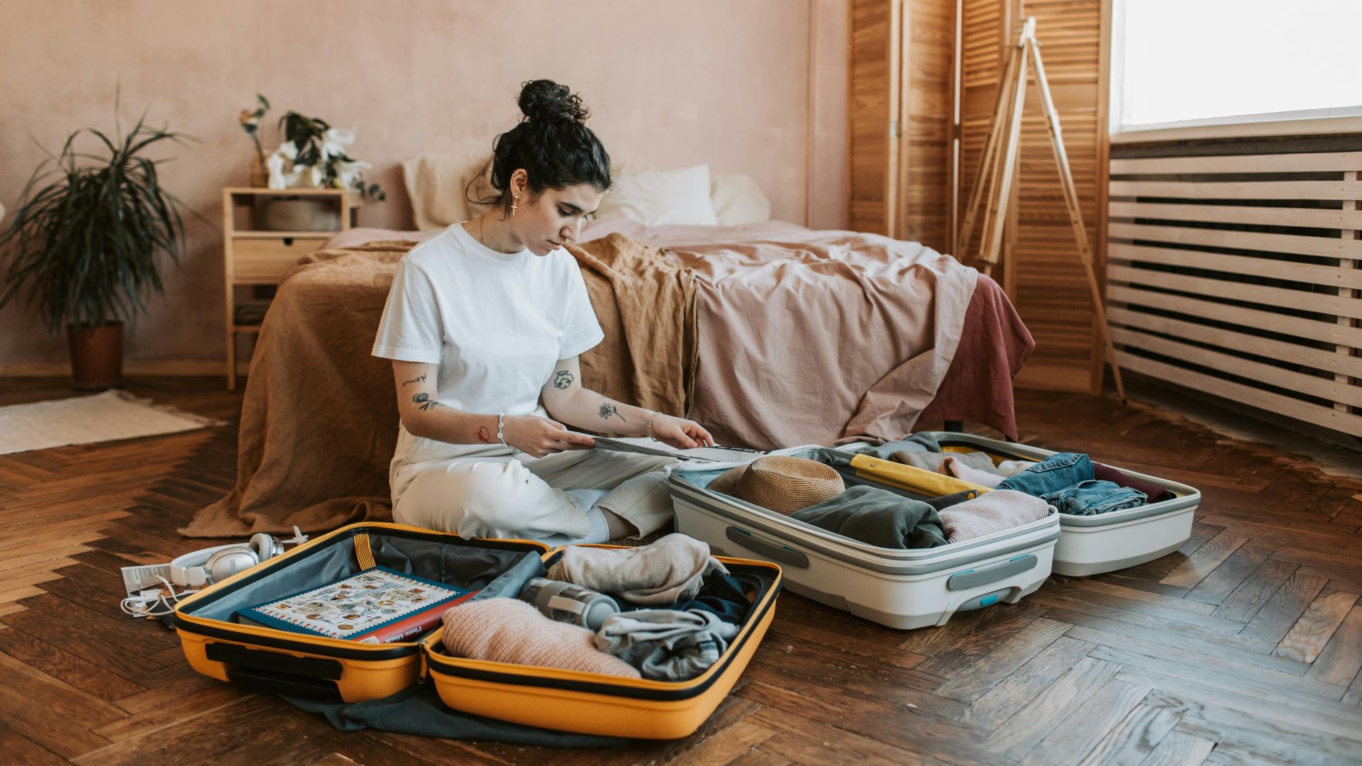 A woman organizes luggage in a stylish bedroom, carrying wanderlust vibes.