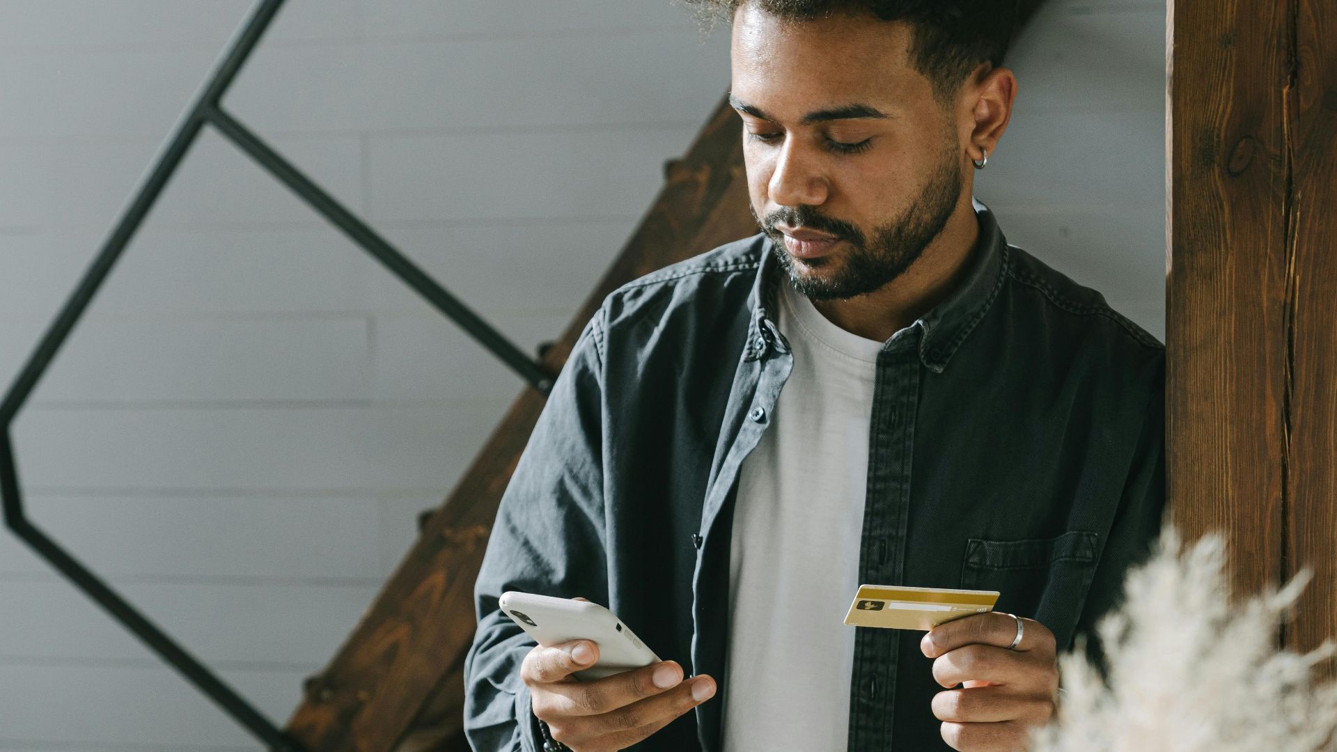 Man using smartphone and card for an online payment in a modern indoor setting.