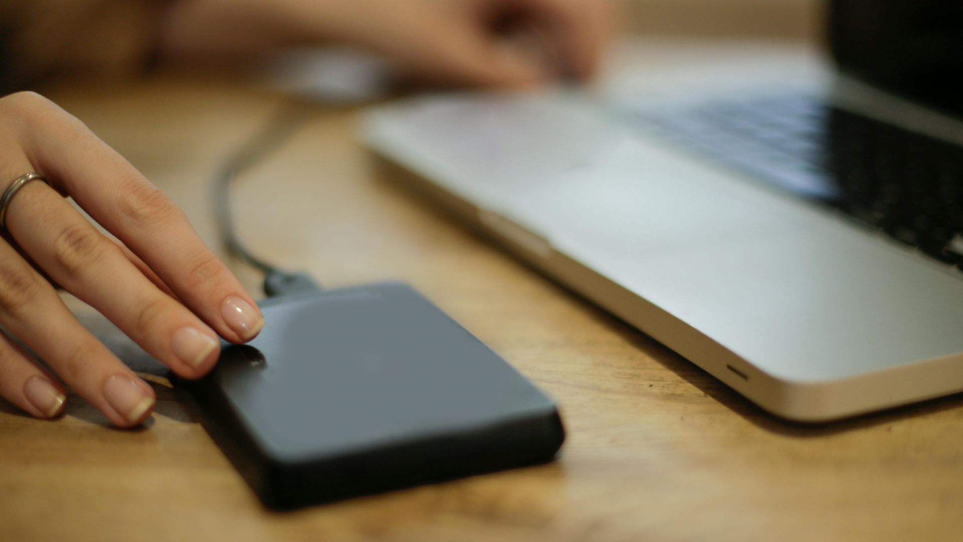 Close-up of a person connecting an external hard drive to a laptop on a desk.