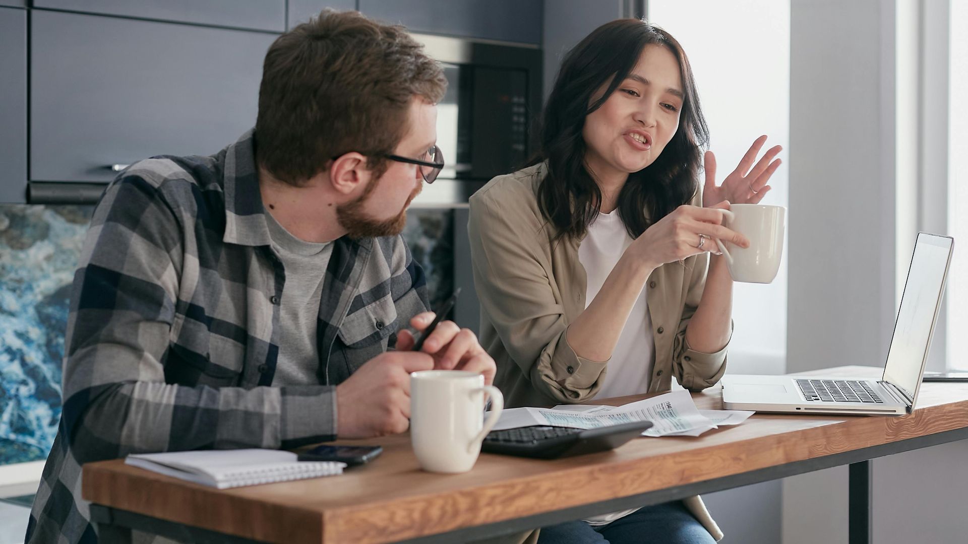 A couple having a discussion with coffee and laptops, reflecting relationship communication indoors.
