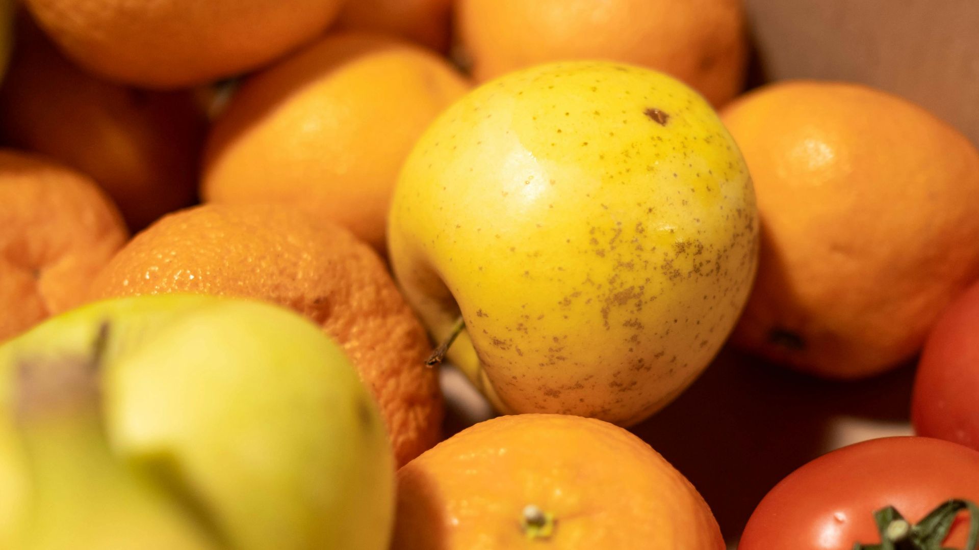 Fresh oranges, bananas, apples, and tomatoes artfully arranged in a cardboard box.
