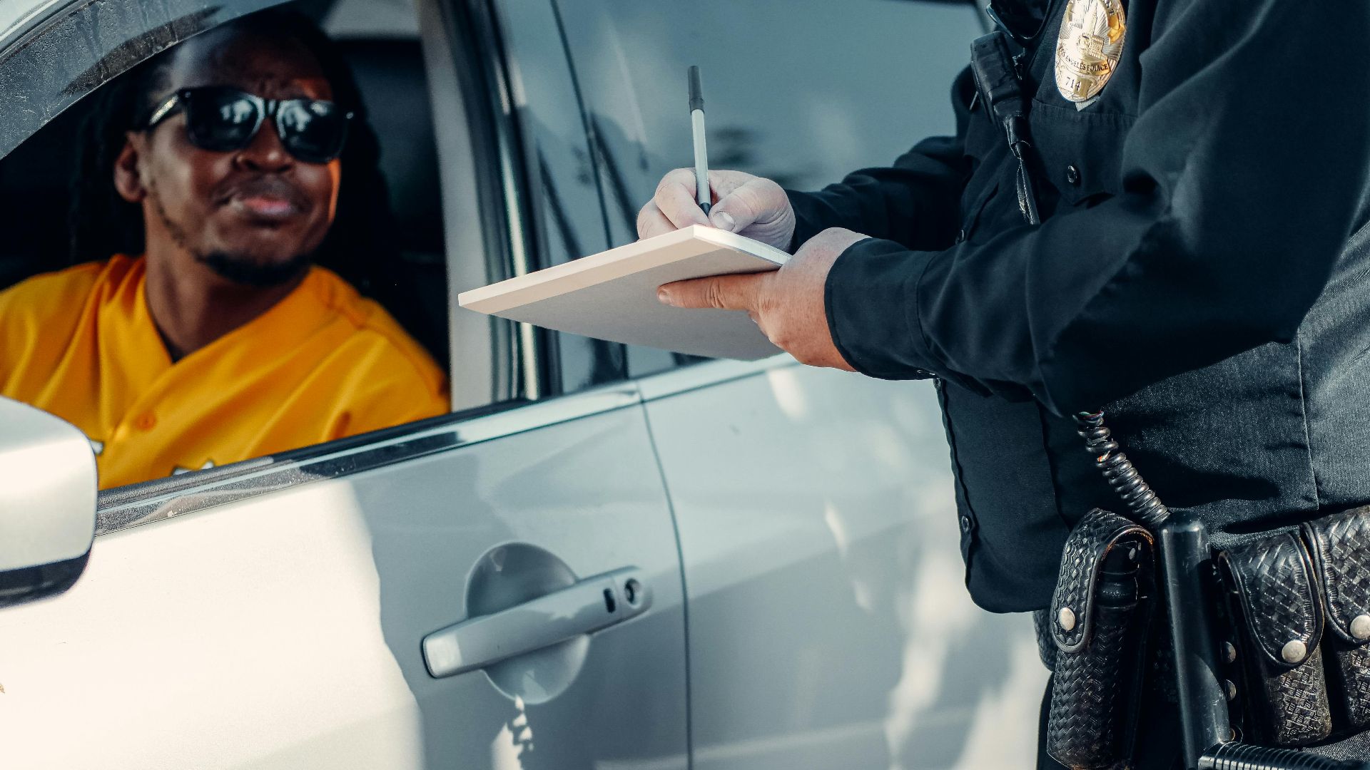 A police officer writes a ticket for a driver in a car during a roadside stop.