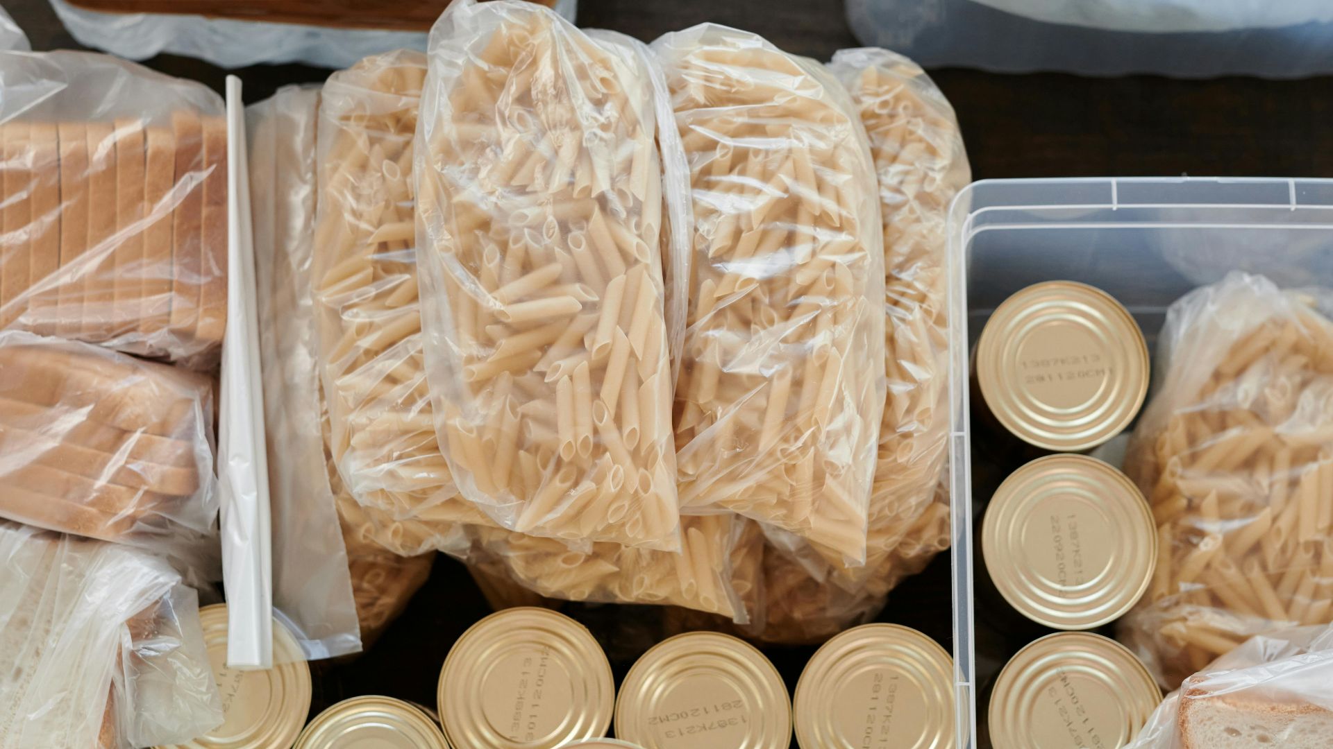 Aerial shot of pantry essentials including pasta, canned food, and bread packaged in plastic bags.
