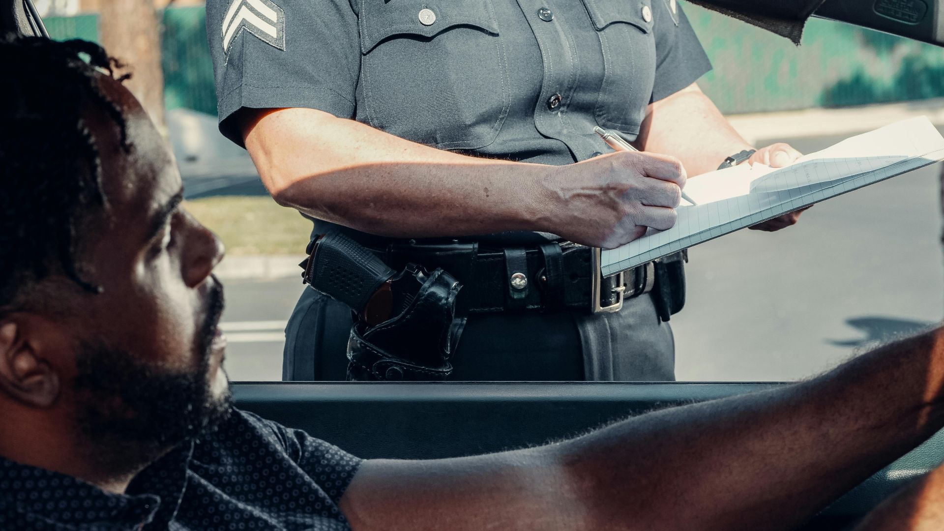 A police officer issues a traffic ticket to a driver seated in a car during the day.