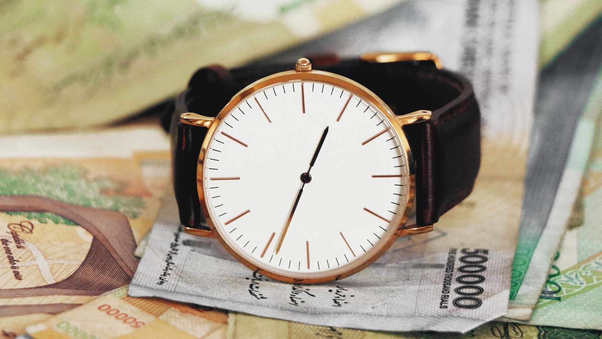 A sophisticated wristwatch resting atop Iranian rial notes, symbolizing time's value in Tehran.
