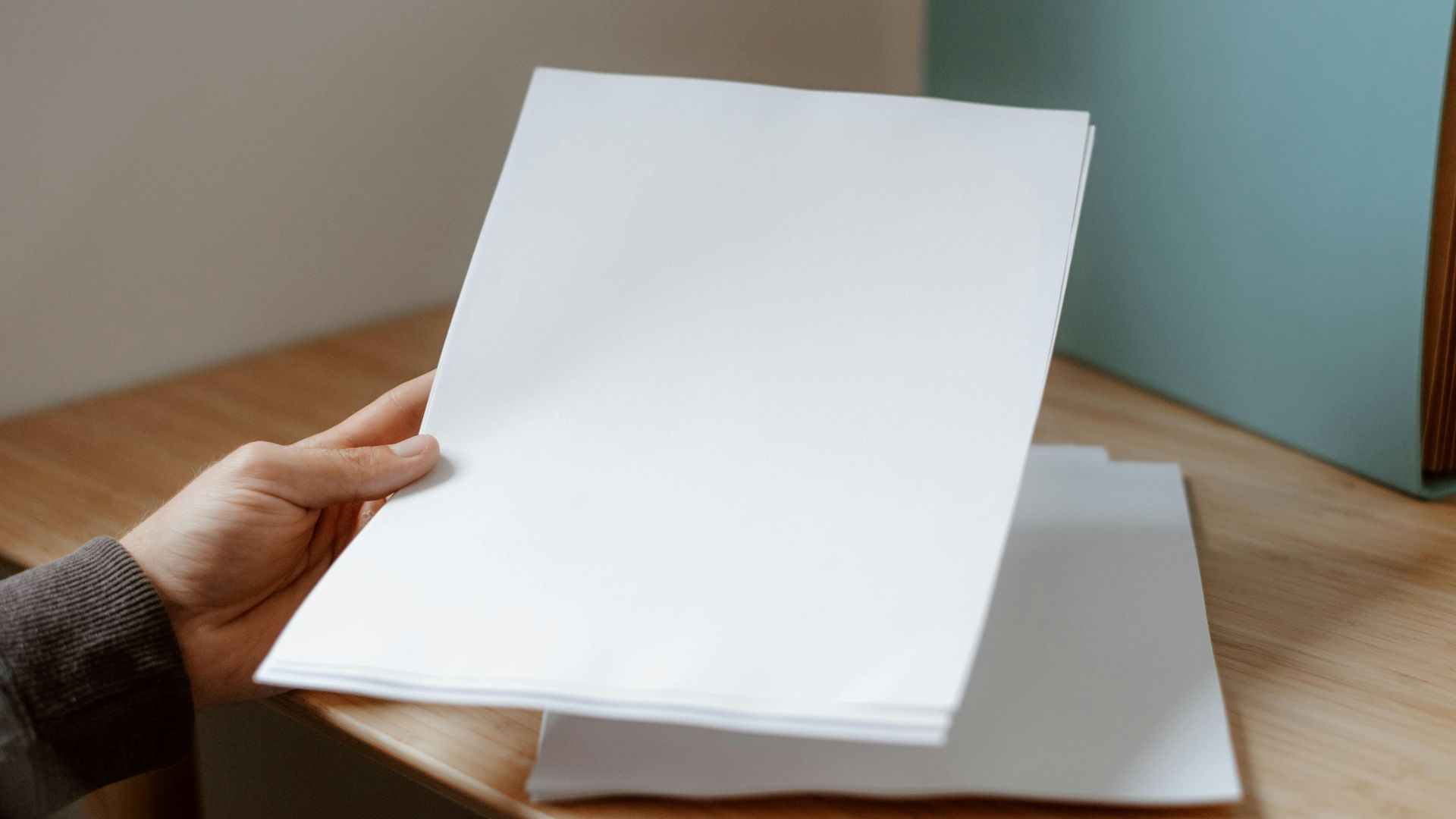 Crop anonymous person demonstrating empty sheet of paper against wooden table with folder for documents
