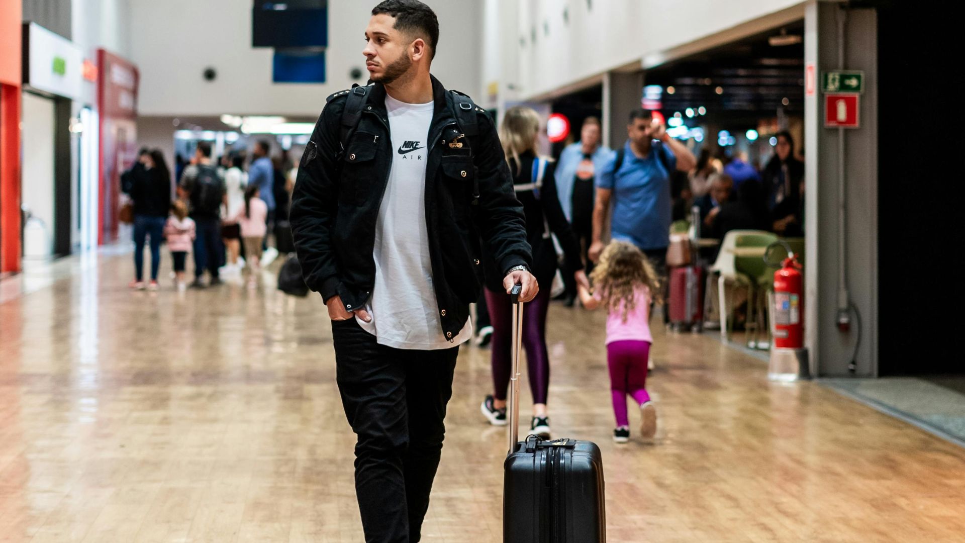 Man walking with luggage in a crowded airport terminal, heading to boarding gates.
