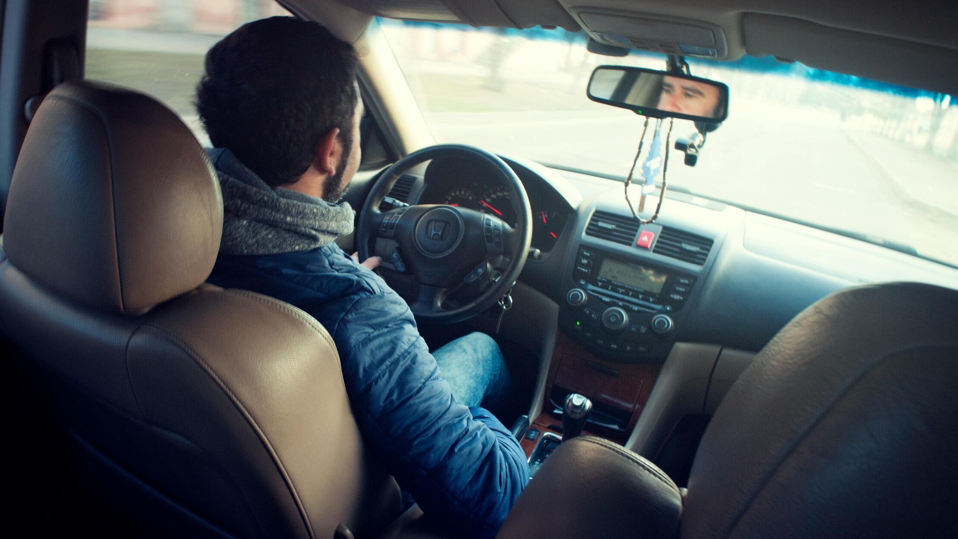 A man driving a car with focus on interior, dashboard, and steering wheel, captured from the backseat.