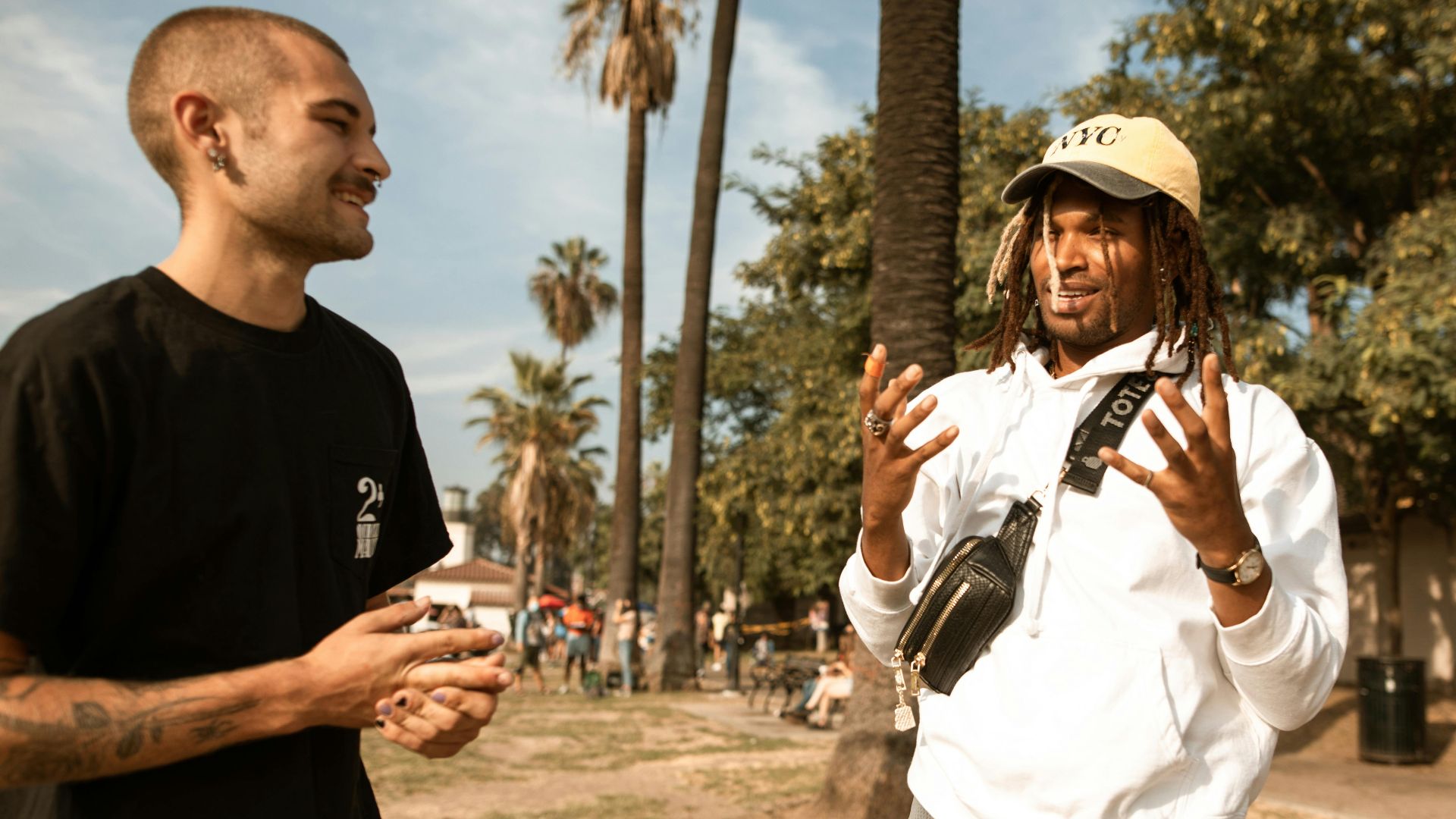 Two friends enjoy a lively conversation in a sunny park surrounded by palm trees.
