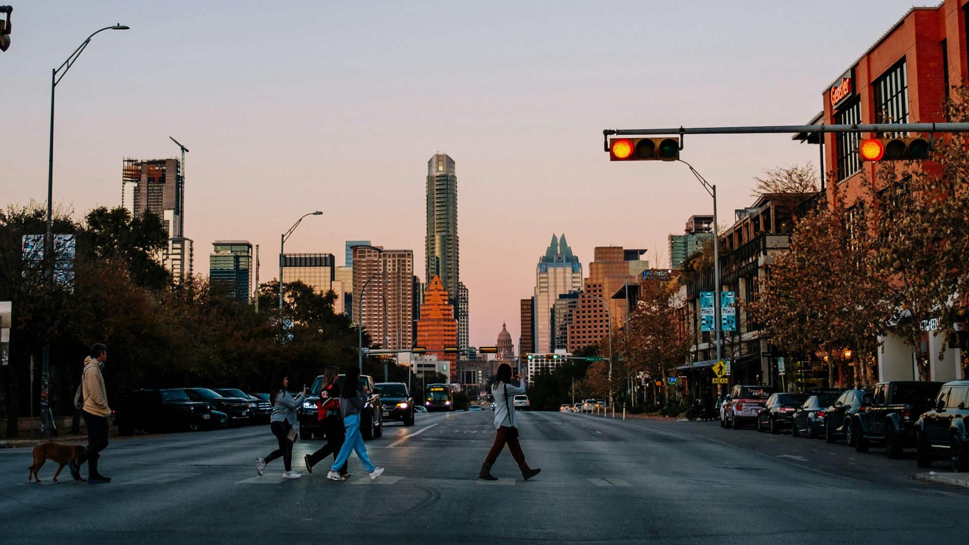 People crossing a city street in Austin, Texas at sunset with the skyline in the background.