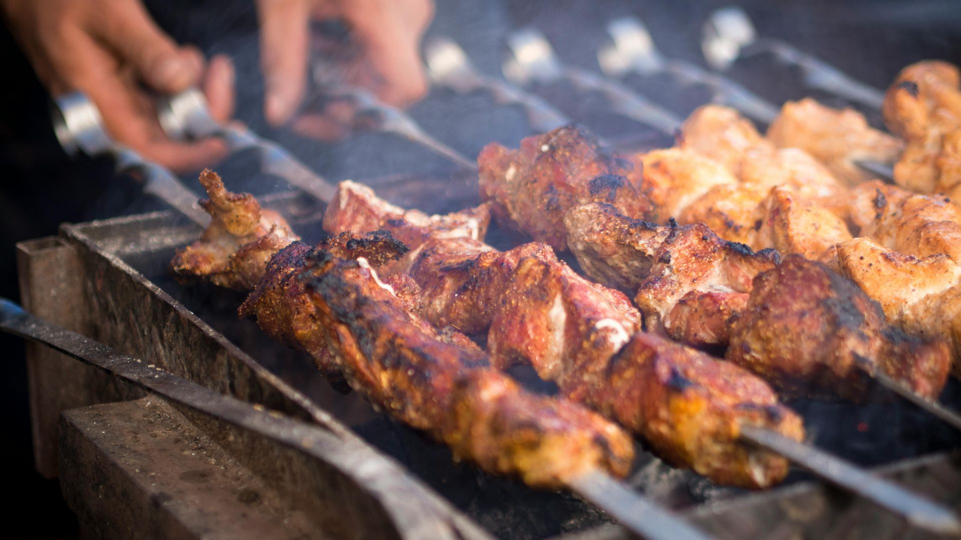 Close-up of skewered meat sizzling on a charcoal grill during an outdoor barbecue.