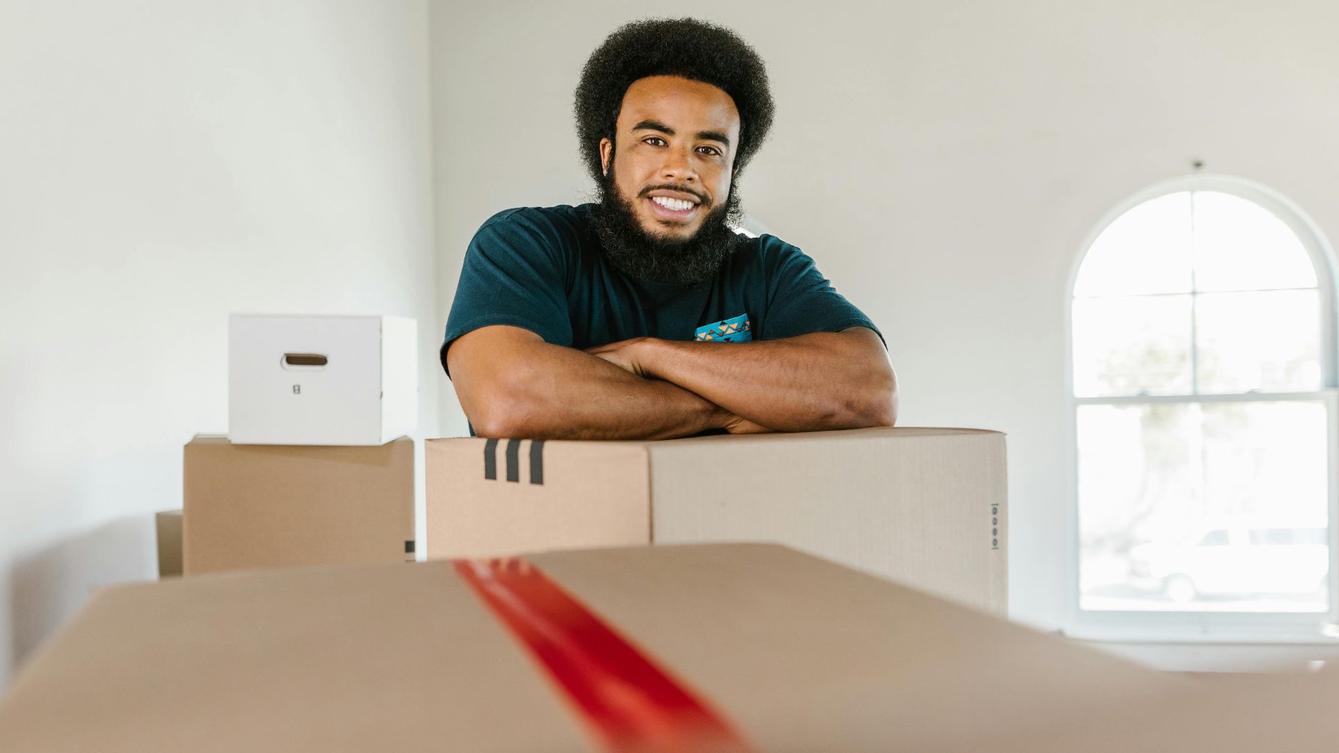 A cheerful mover standing with packed boxes indoors, ready for a moving day.