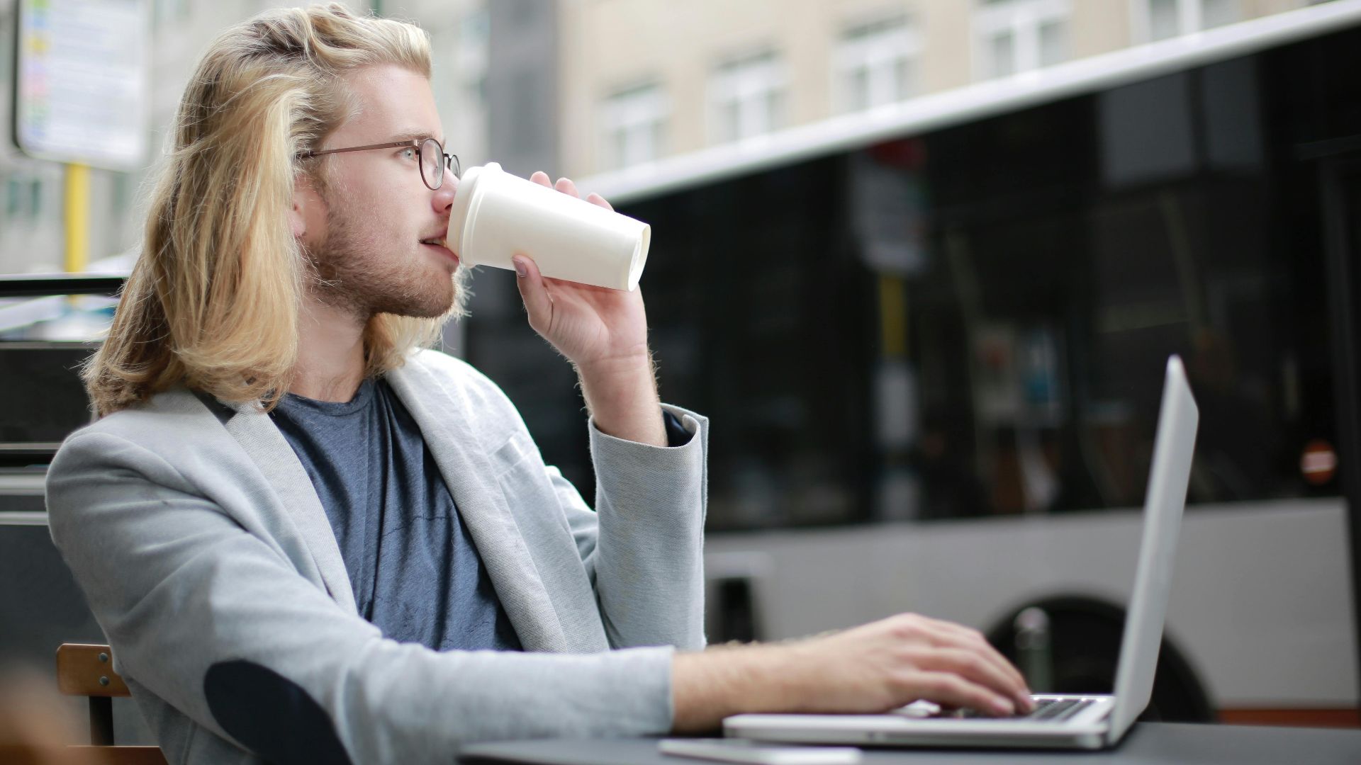 Young man working remotely on laptop while enjoying a coffee outdoors.