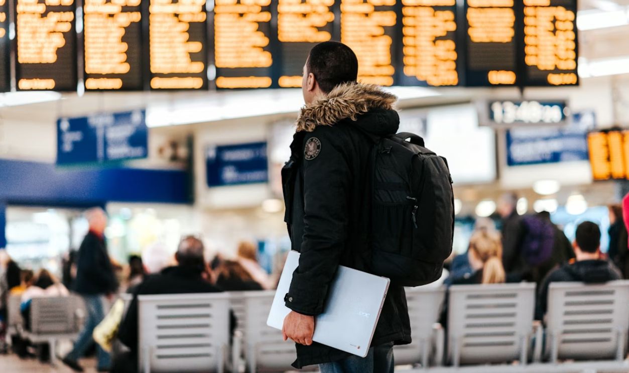 man standing inside airport looking at LED flight schedule bulletin board