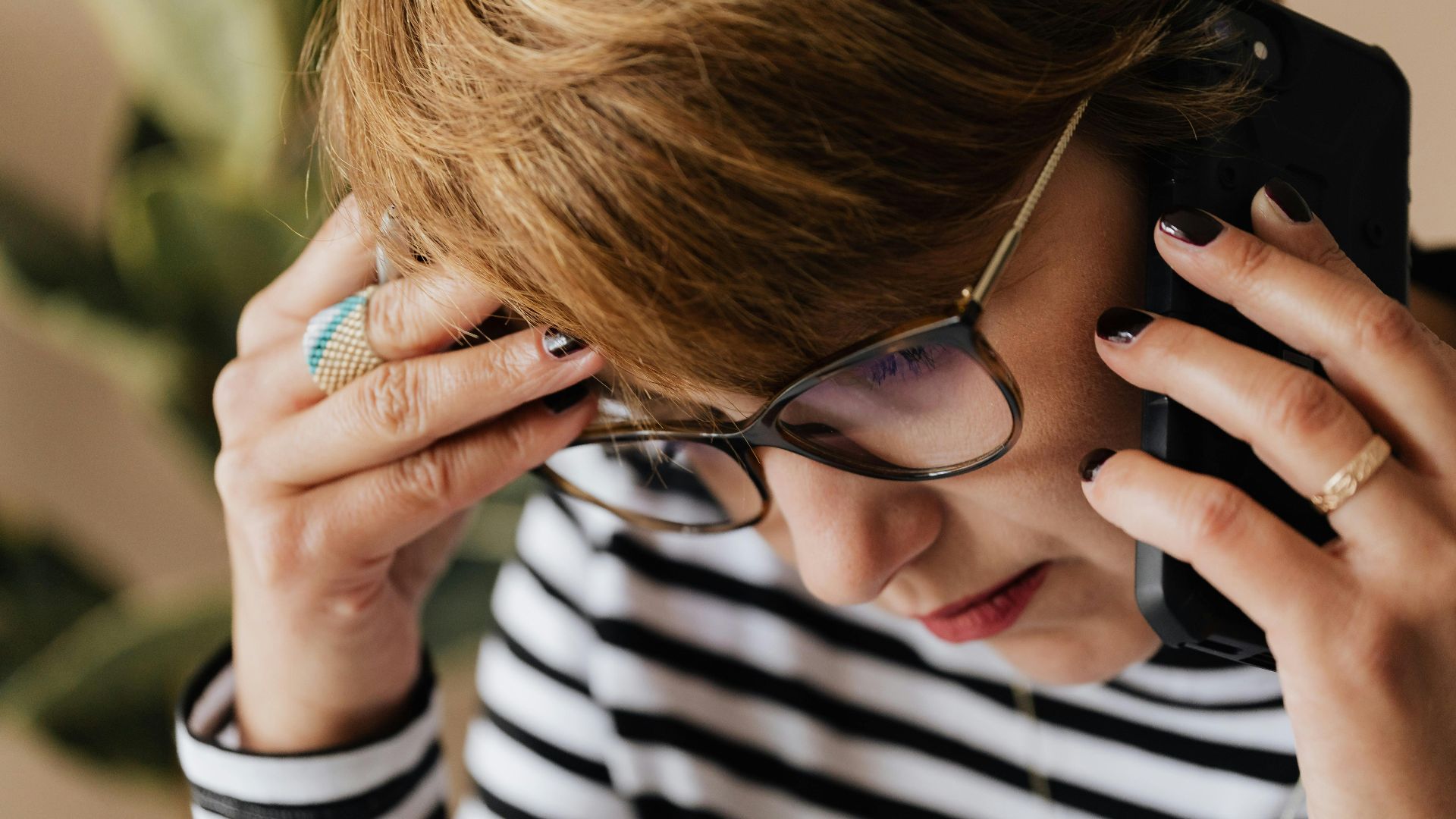 Focused woman with eyeglasses discussing work over a phone call, looking concerned and thoughtful.