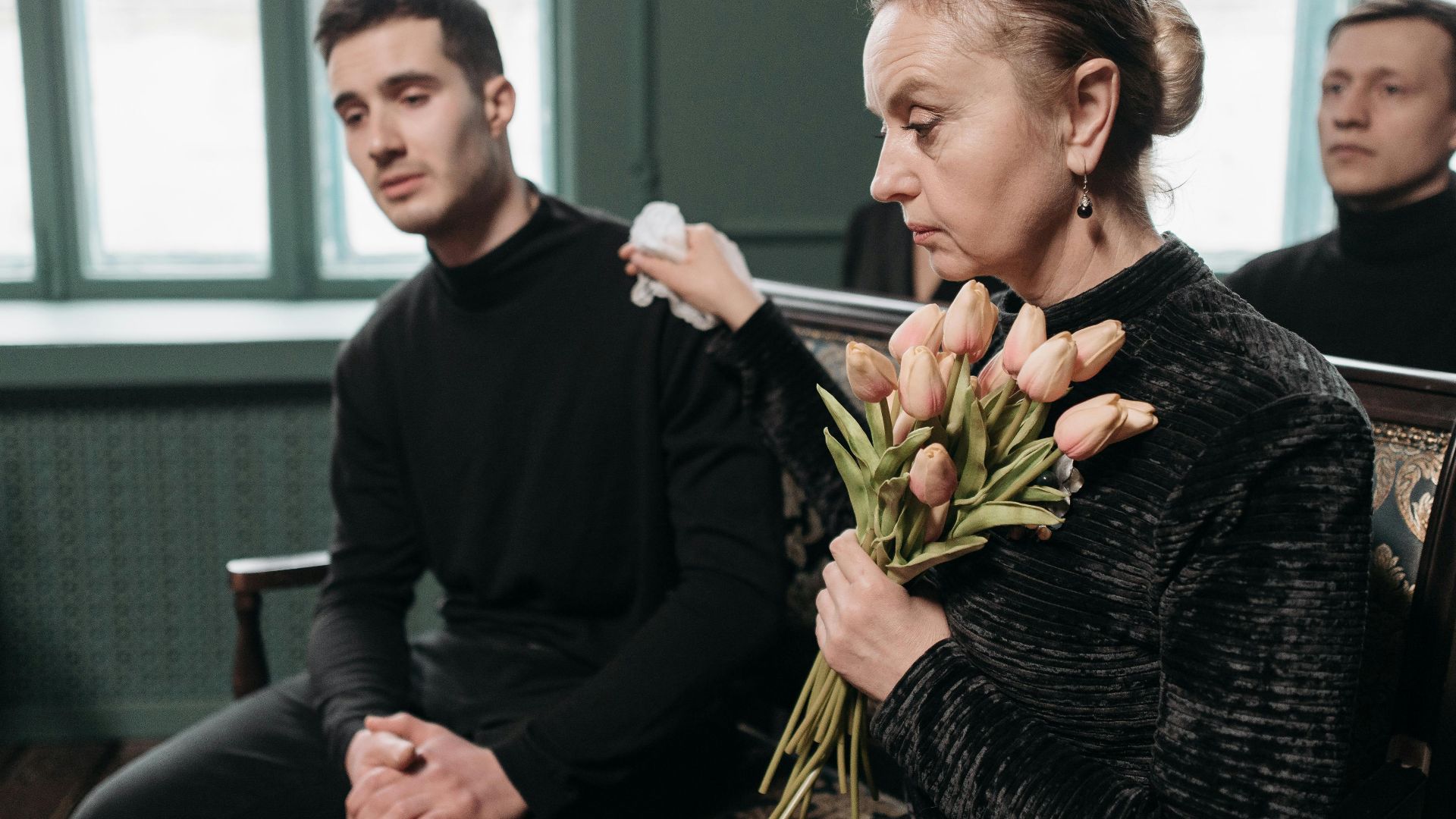 Family members mourning at a funeral, holding flowers, expressing grief.