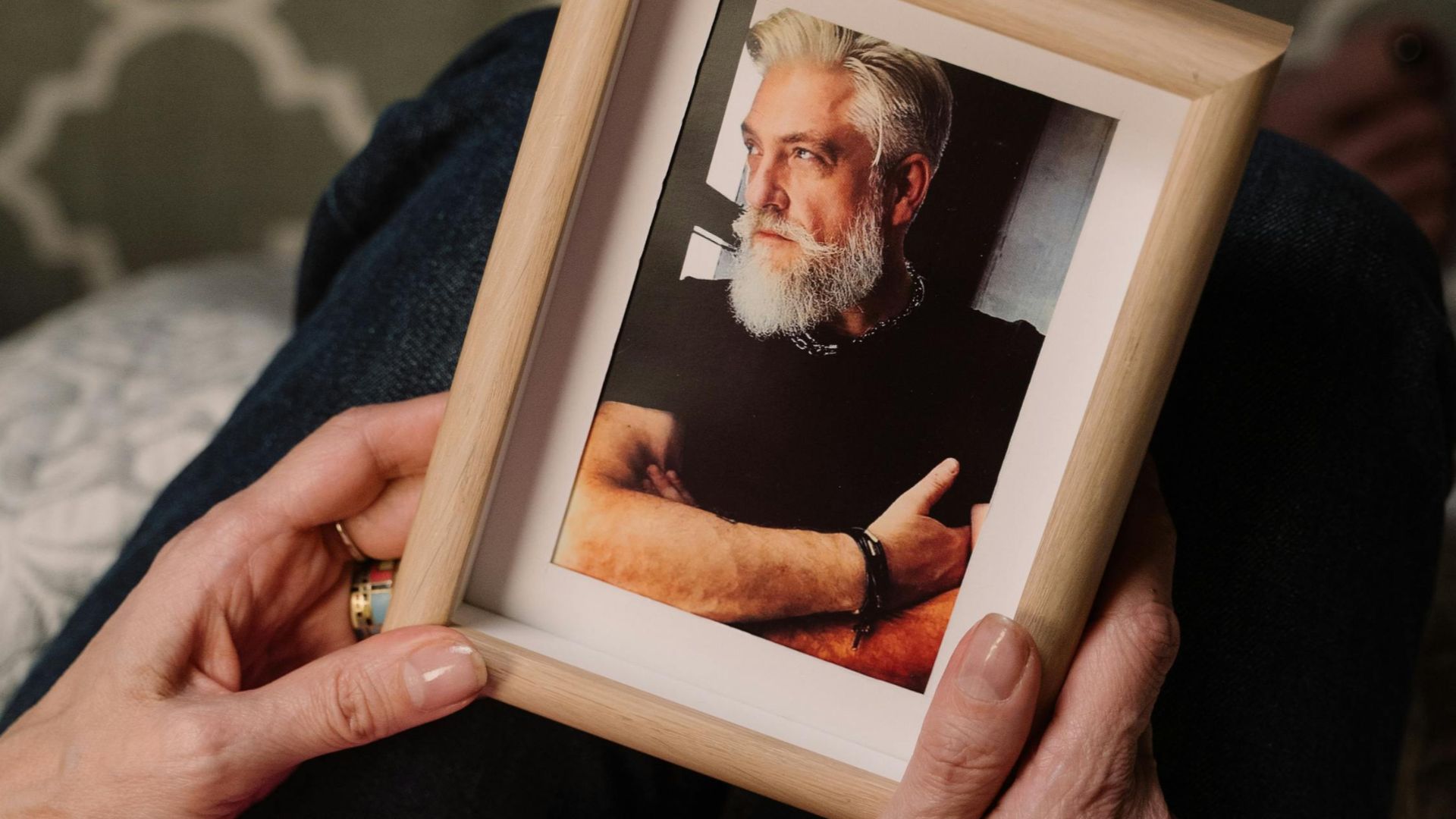 A woman in a pink shirt holds a wooden frame with a man's portrait.