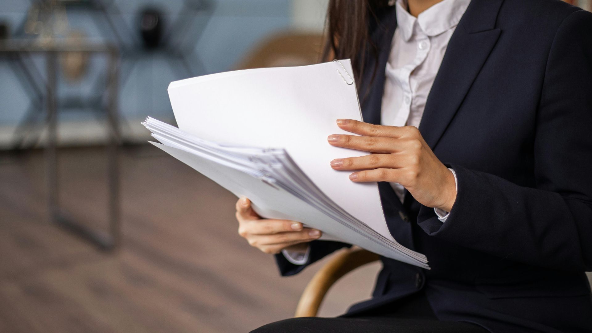 A professional woman in a suit reviewing documents while seated in an elegant office setting.