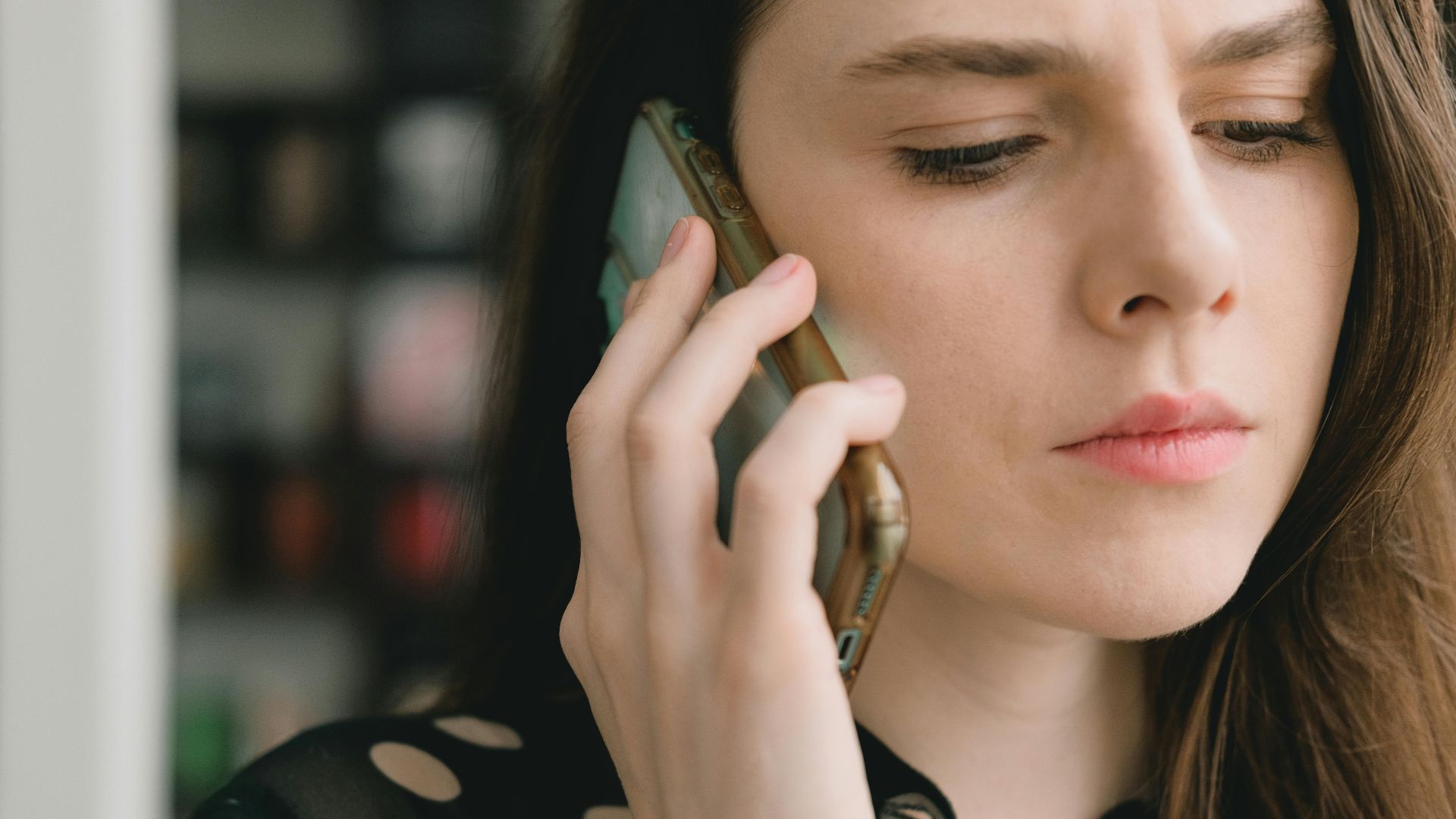 Close-up of a woman engaged in a phone conversation indoors, depicting a thoughtful expression.