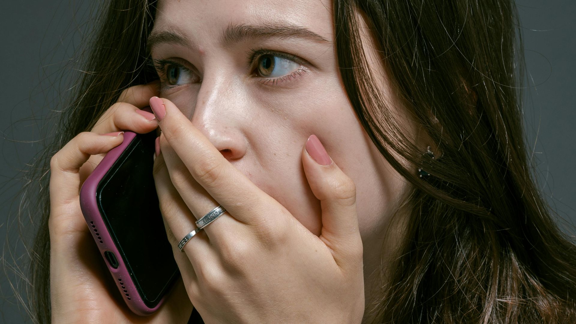 A concerned woman talking on the phone, covering her mouth with her hand, showing emotional distress.