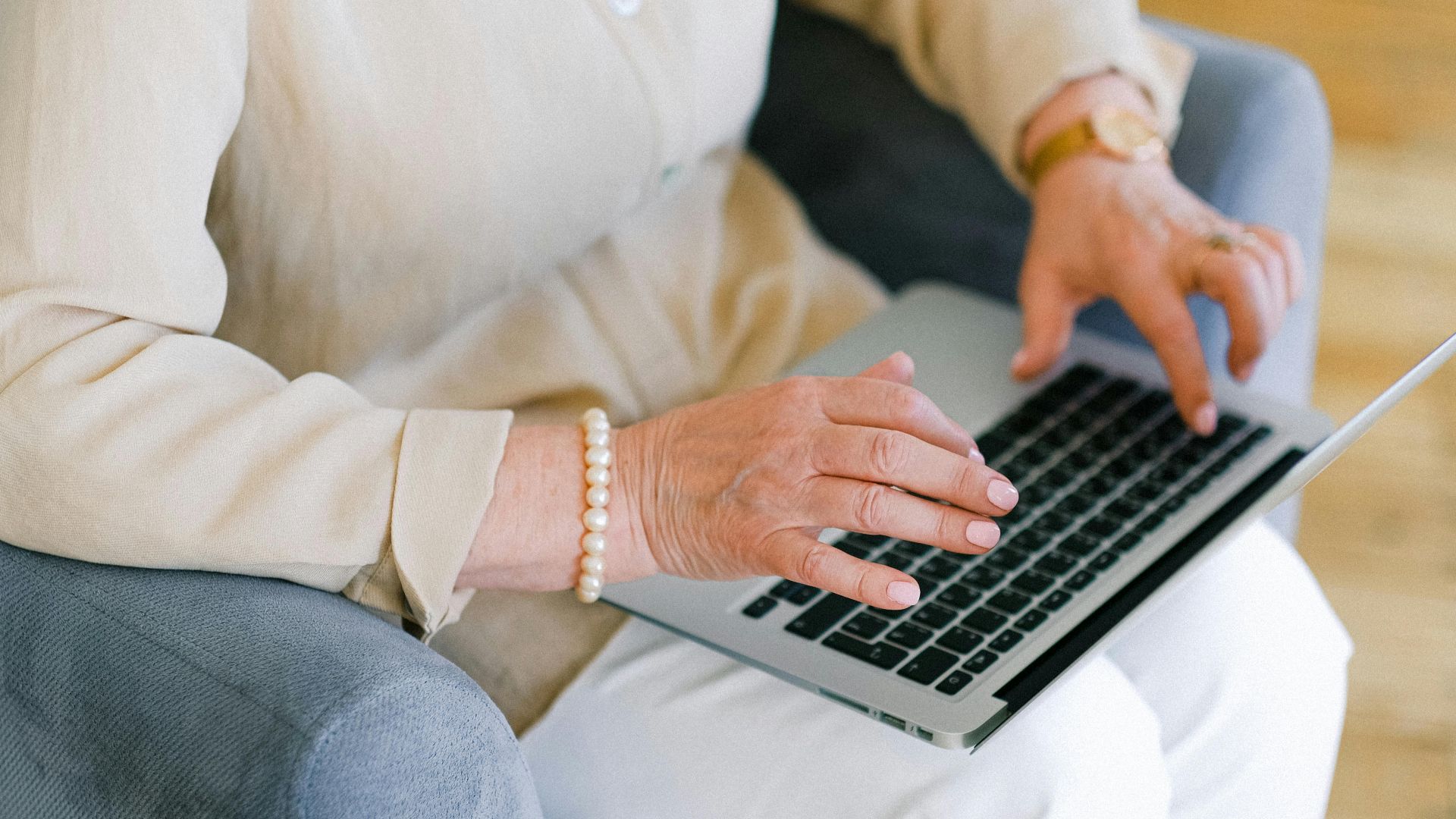 Senior woman typing on a laptop while sitting in a cozy armchair indoors.
