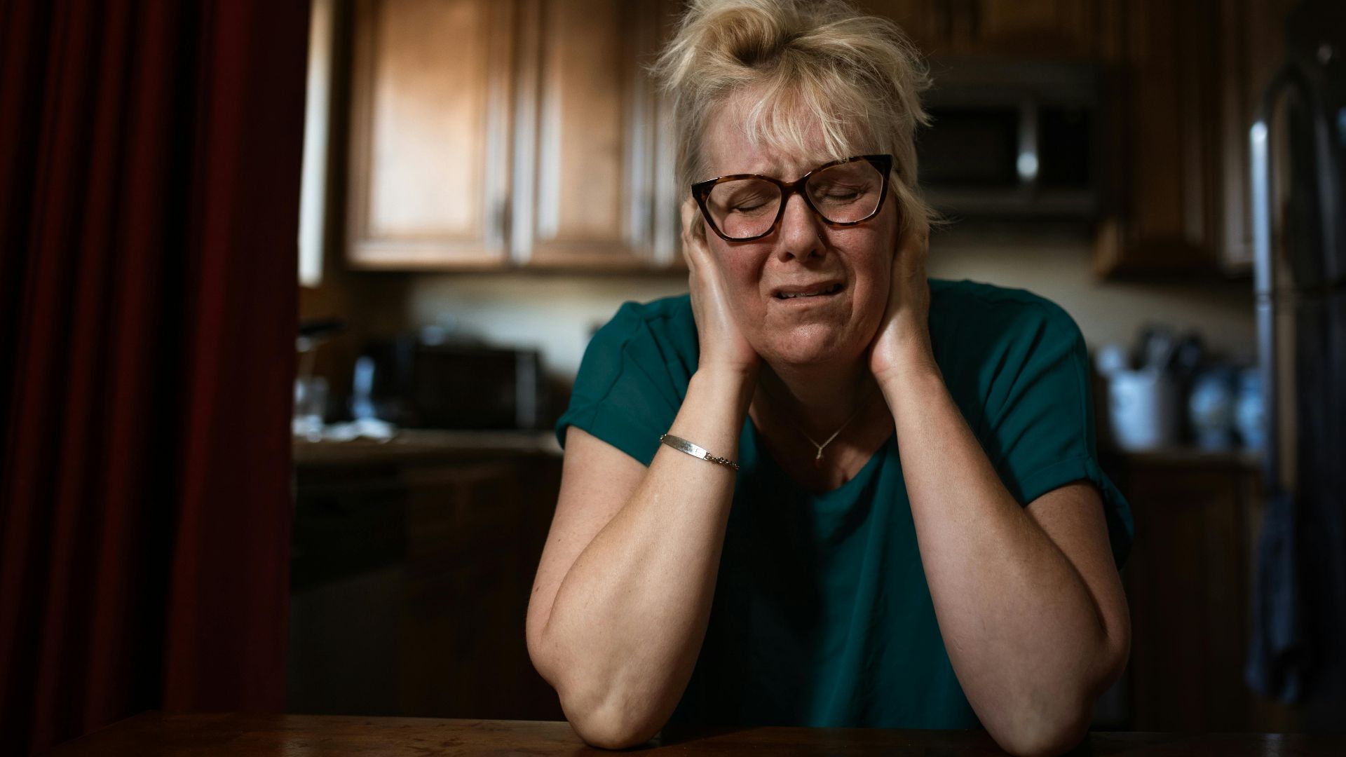 An adult woman in distress sitting at a table indoors, conveying emotional struggle.