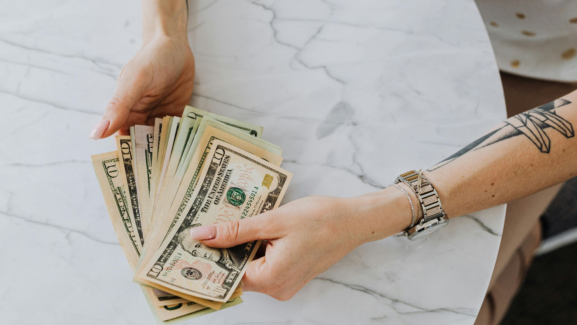 Hands holding and counting US dollar bills on a marble table, depicting wealth and finance.