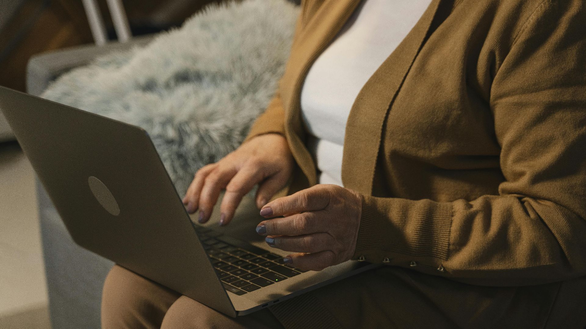 A senior adult using a laptop on a sofa, working comfortably in a home setting.
