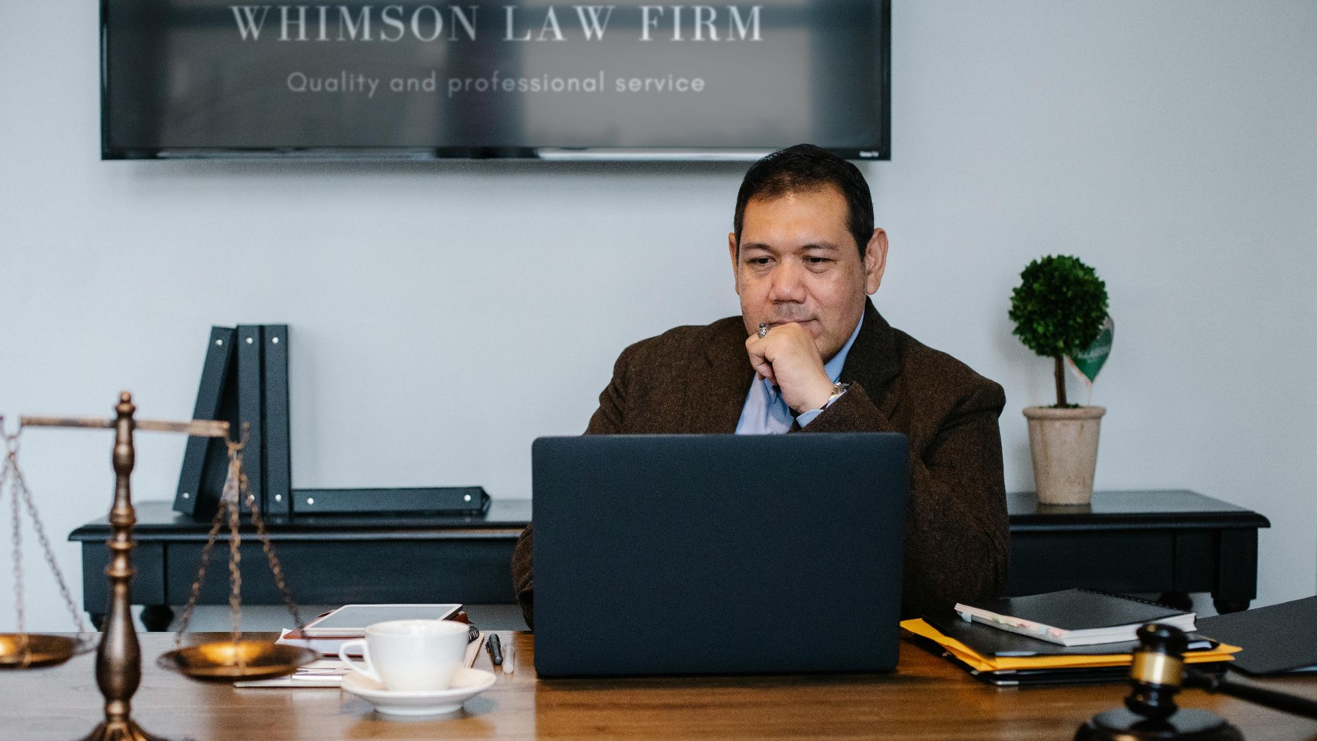 Serious ethnic mature man in formal outfit working with netbook at table with gavel