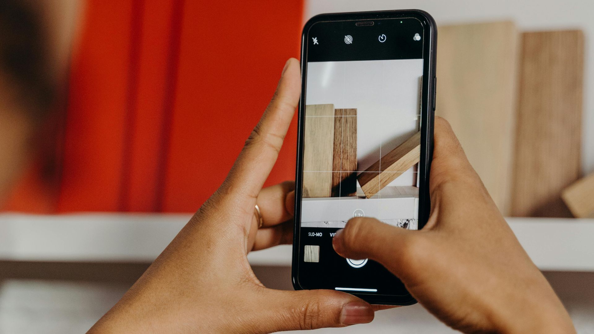 Close-up of hands holding a smartphone to photograph books on a shelf indoors.