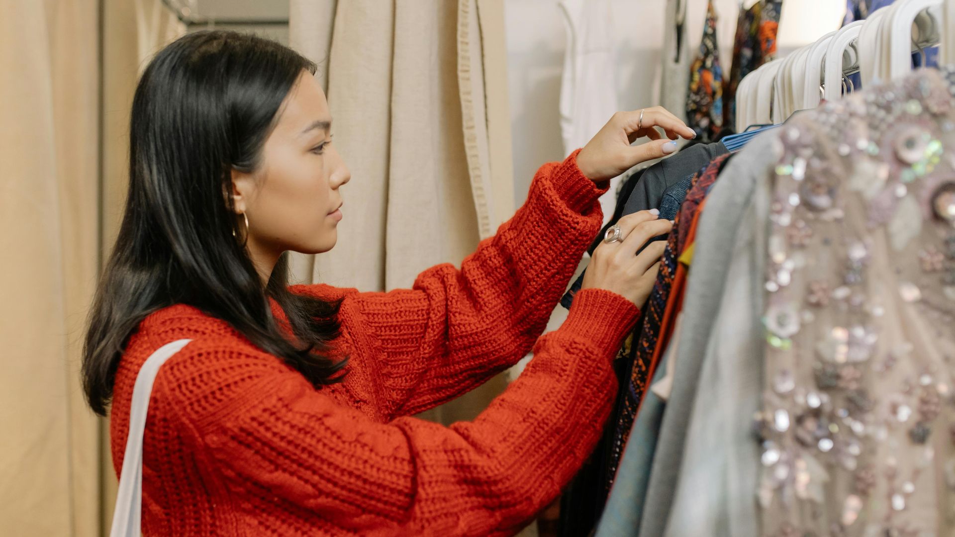 A fashionable Asian woman chooses clothes from a rack in a store, emphasizing style and choice.